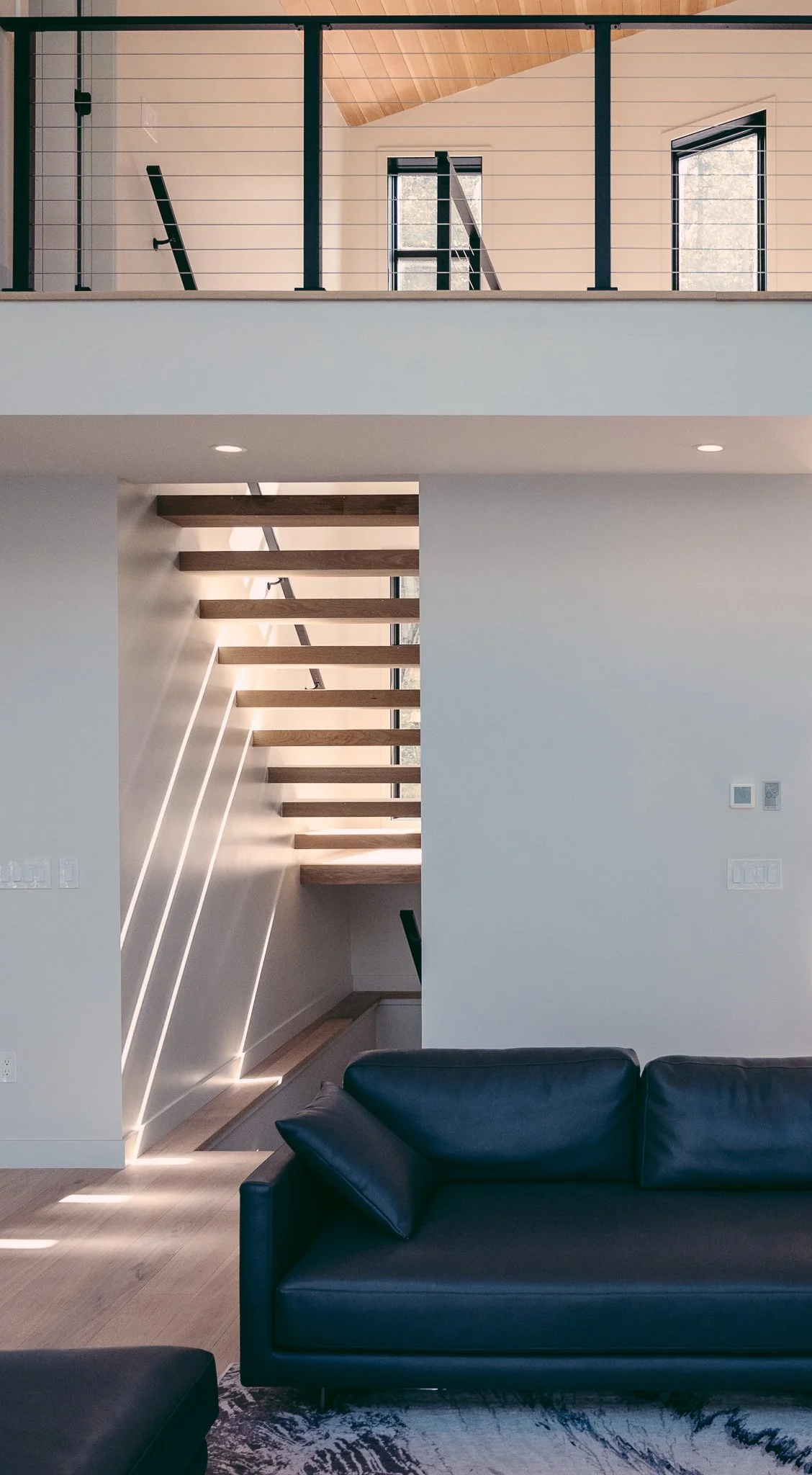 Open stair with floating wood treads and a cable-railing loft above a living space