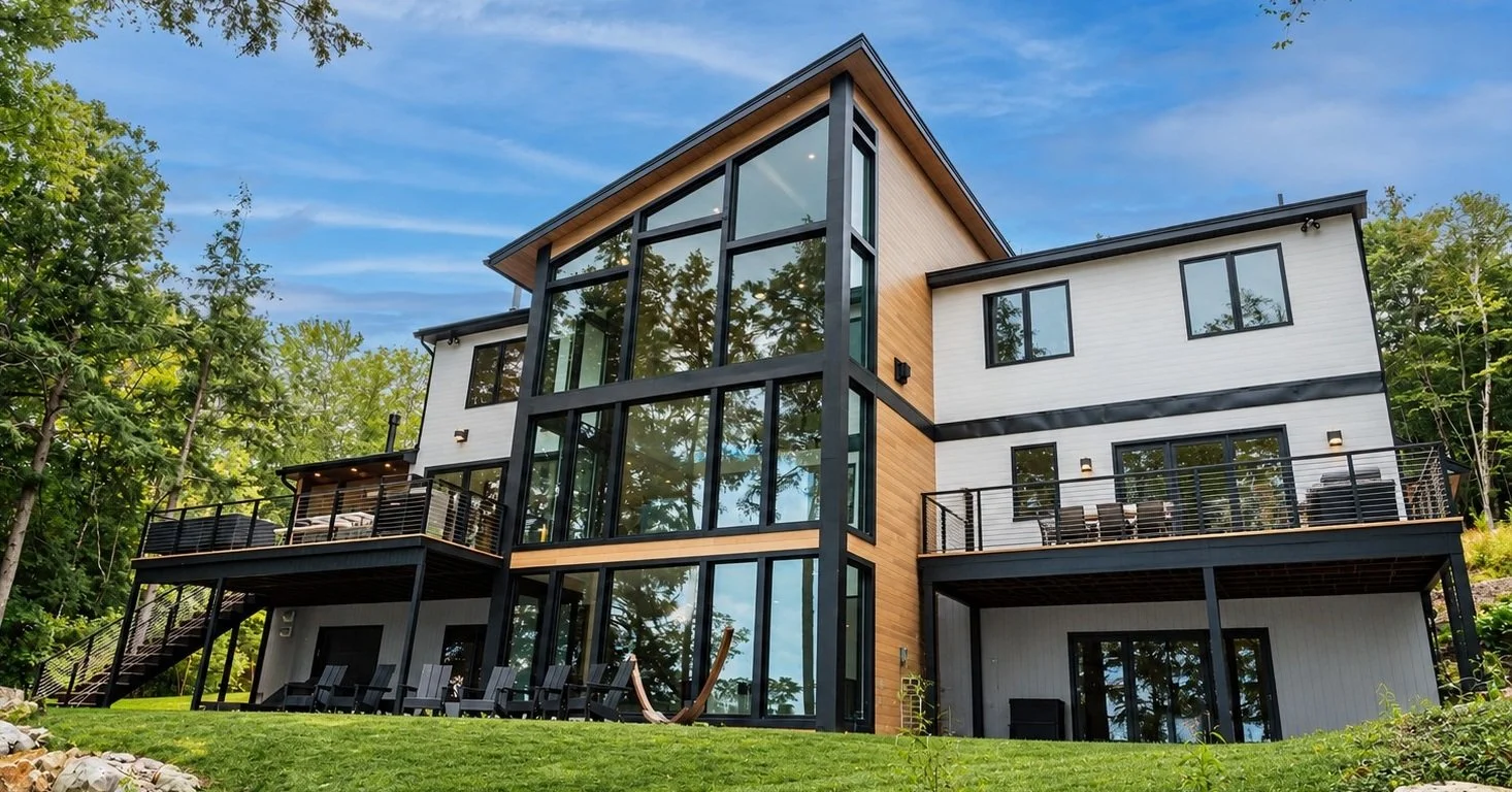 Lake side of the house with a wall of black-framed windows, two decks, and a green lawn