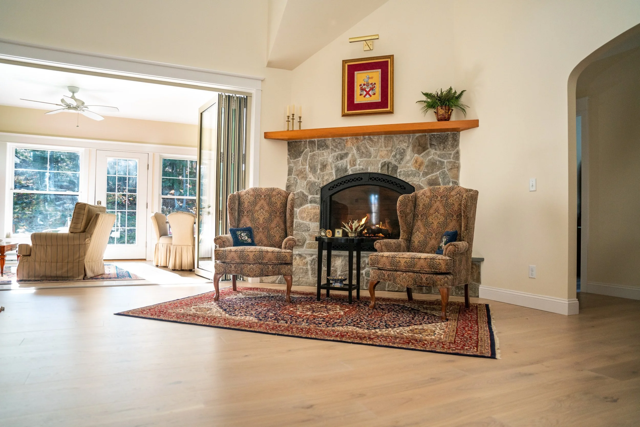 Stone gas fireplace with a wood mantel and the accordion door folded open to the sunroom