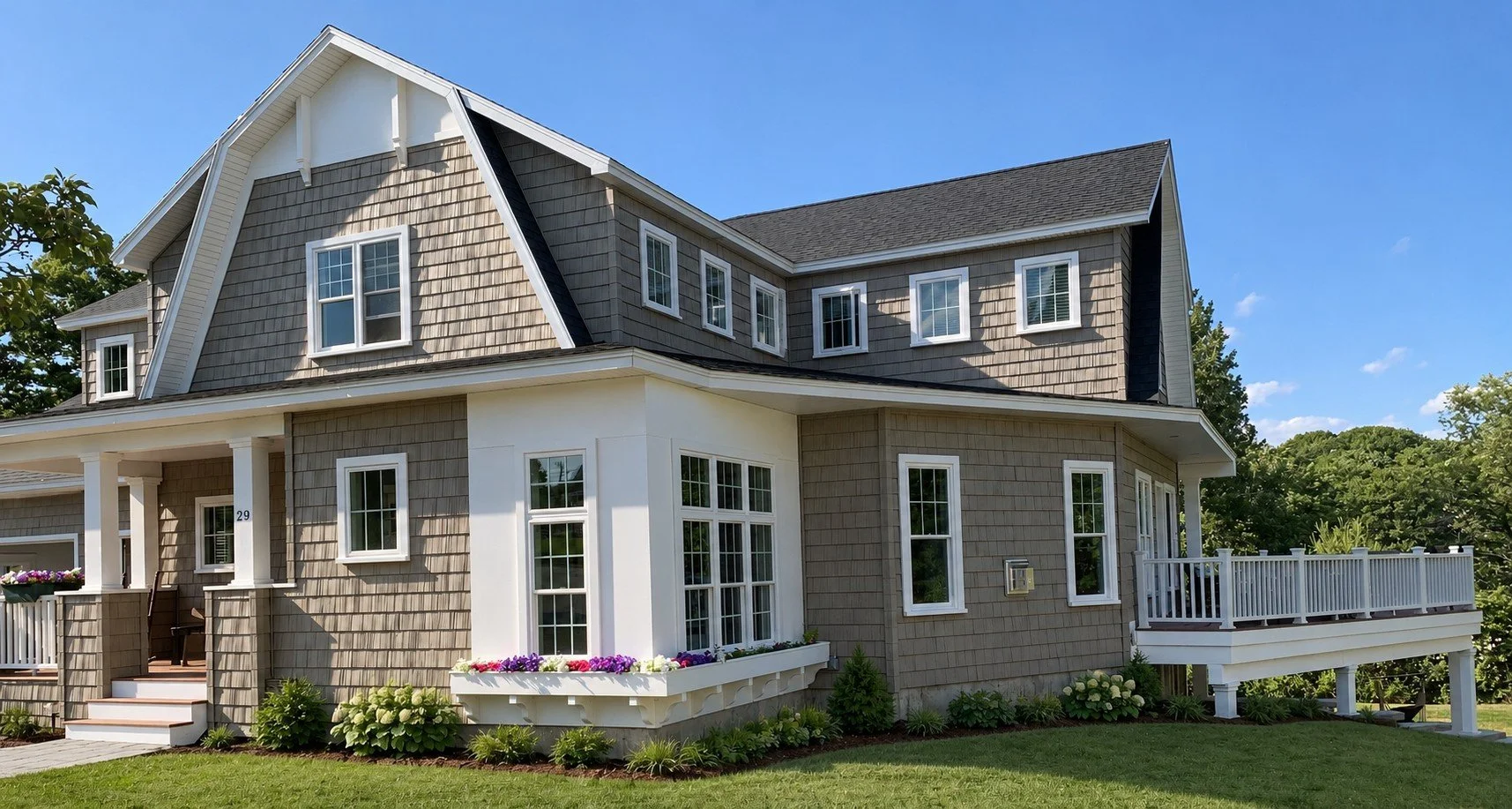 Side of the gray shingle-style home with a gambrel roof, wraparound porch, and a deck over a green lawn