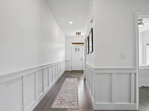 Wide hallway with raised panel wainscot and a runner rug leading to the front door