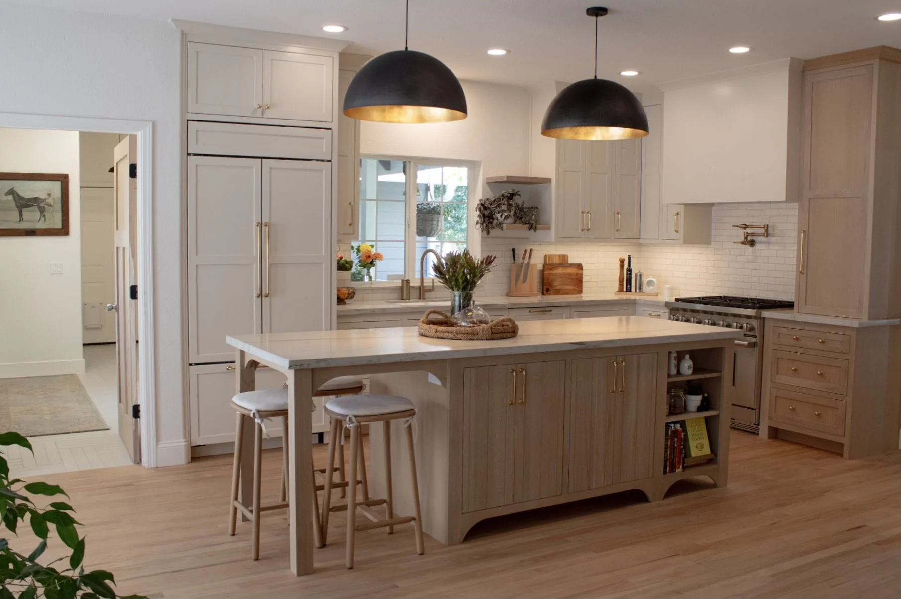 Modern kitchen with white cabinetry, a kitchen island with a marble countertop, black pendant lights with gold interior, and wooden flooring.