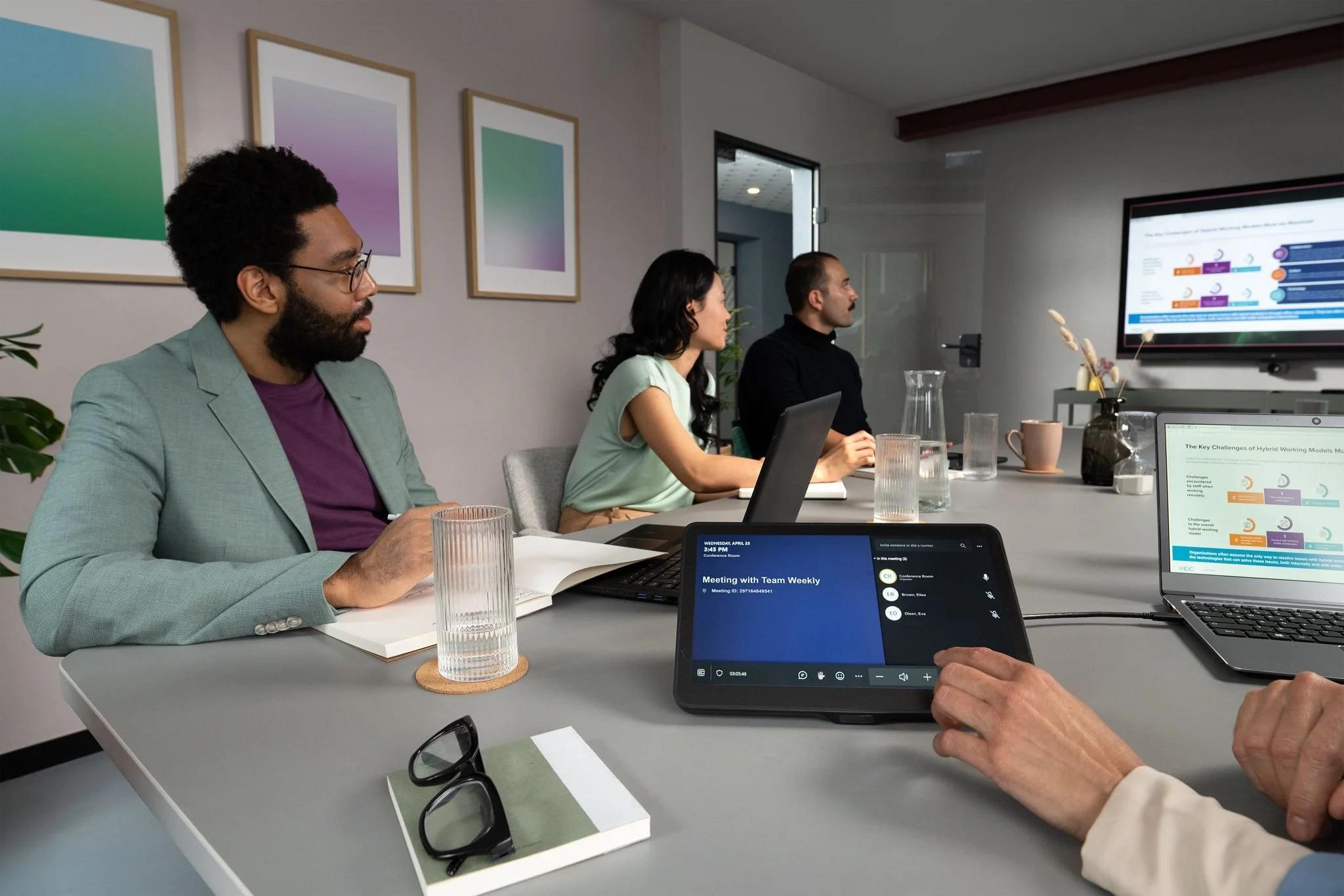 People attending a business meeting in a conference room with laptops, notebooks, glasses of water, and presentation screens