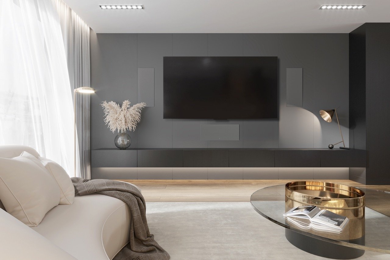 Modern living room with a white couch, a black entertainment center with a large TV, a vase with pampas grass, a brass floor lamp, a glass coffee table with a decorative bowl and book, and light-colored wood flooring with sheer curtains on the window