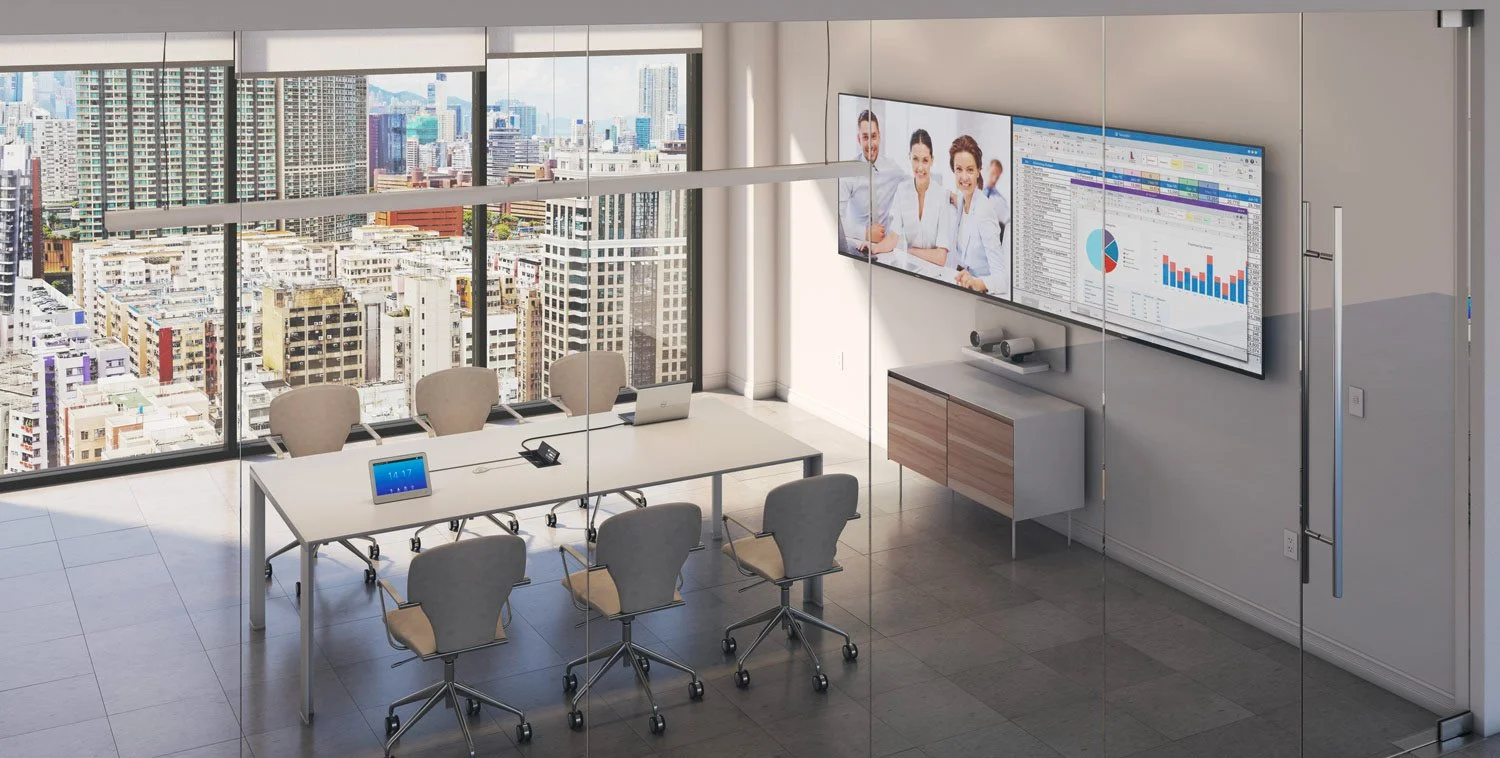 Modern conference room with a long white table, six beige office chairs, a digital tablet, a telephone, and laptops. Large windows show a cityscape of tall buildings. Two wall-mounted screens display a group of professionals and various charts and gr