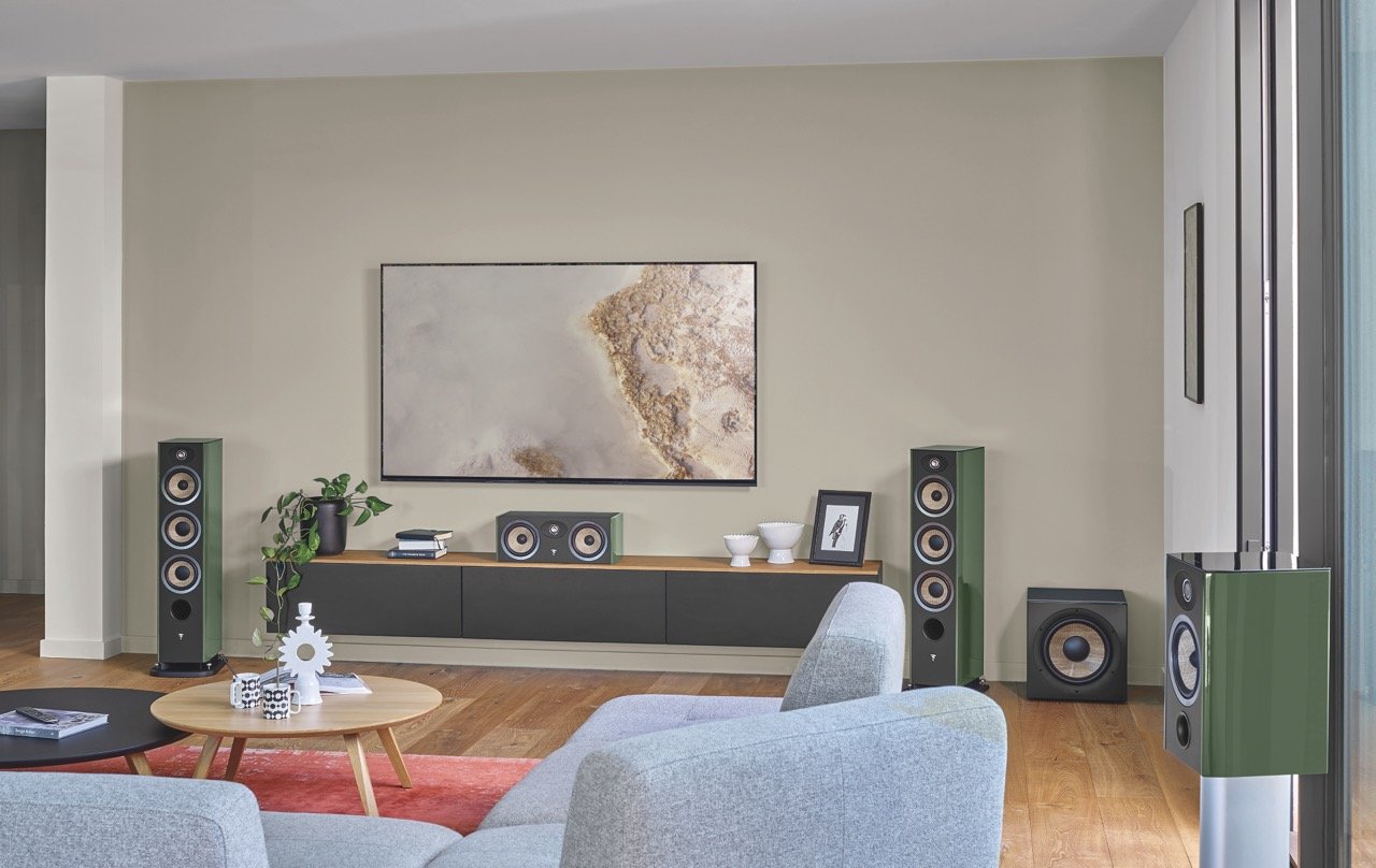 Modern living room with a gray sofa, a wooden coffee table, a large artwork on the wall, and a sound system with tall green speakers, a subwoofer, and a black TV stand with decorative items.