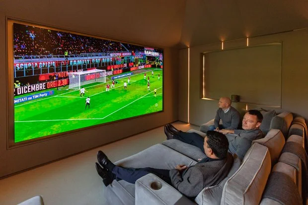 Three men watching a soccer game on a large television Samsung the wall LED screen in a modern, cozy living room.