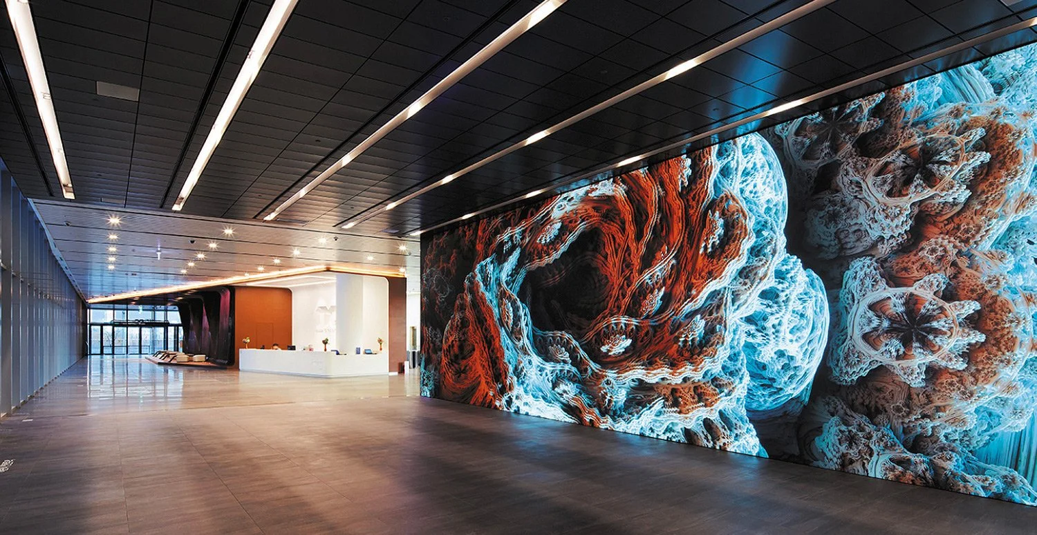 Modern interior with a large illuminated digital mural of sea coral on the wall, a sleek white reception desk, and minimal furniture in a spacious lobby.