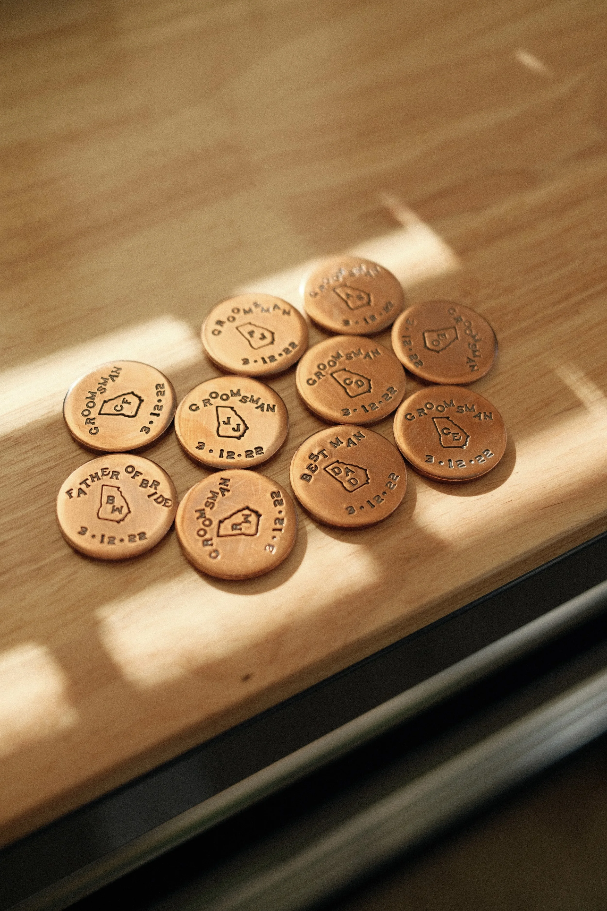 Decorative copper tokens with engraved text and house icon, printed with phrases like 'Groom's Man', 'Father of Bride', 'Best Man', along with a date '3.12.22'.