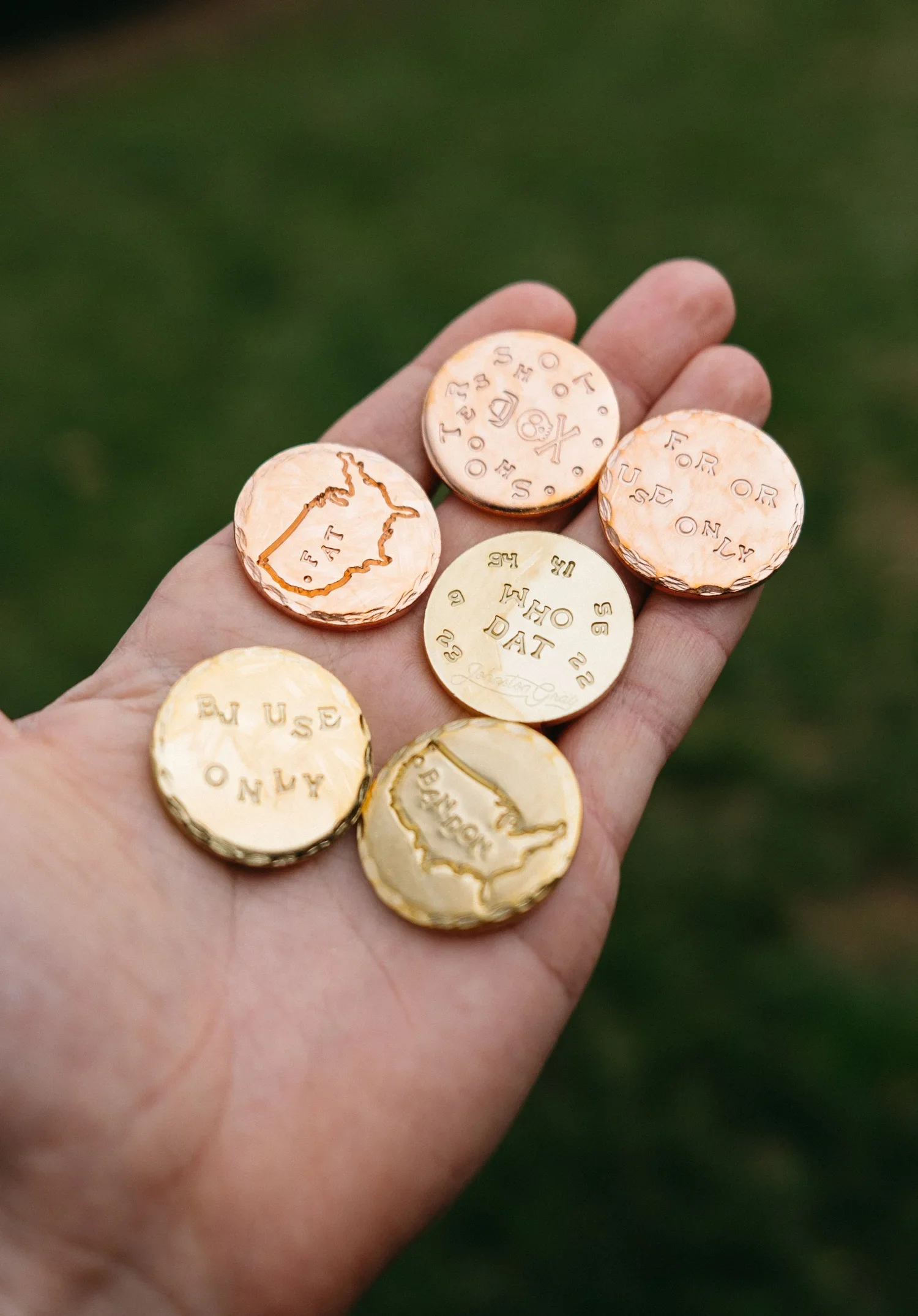Hand holding several gold and copper coins with engraved maps of the United States and the words 'RUSH ONLY', 'FOR USE ONLY', 'WHAT'S MY DAT', 'GOVERNMENT', and 'TO THE BEST.'
