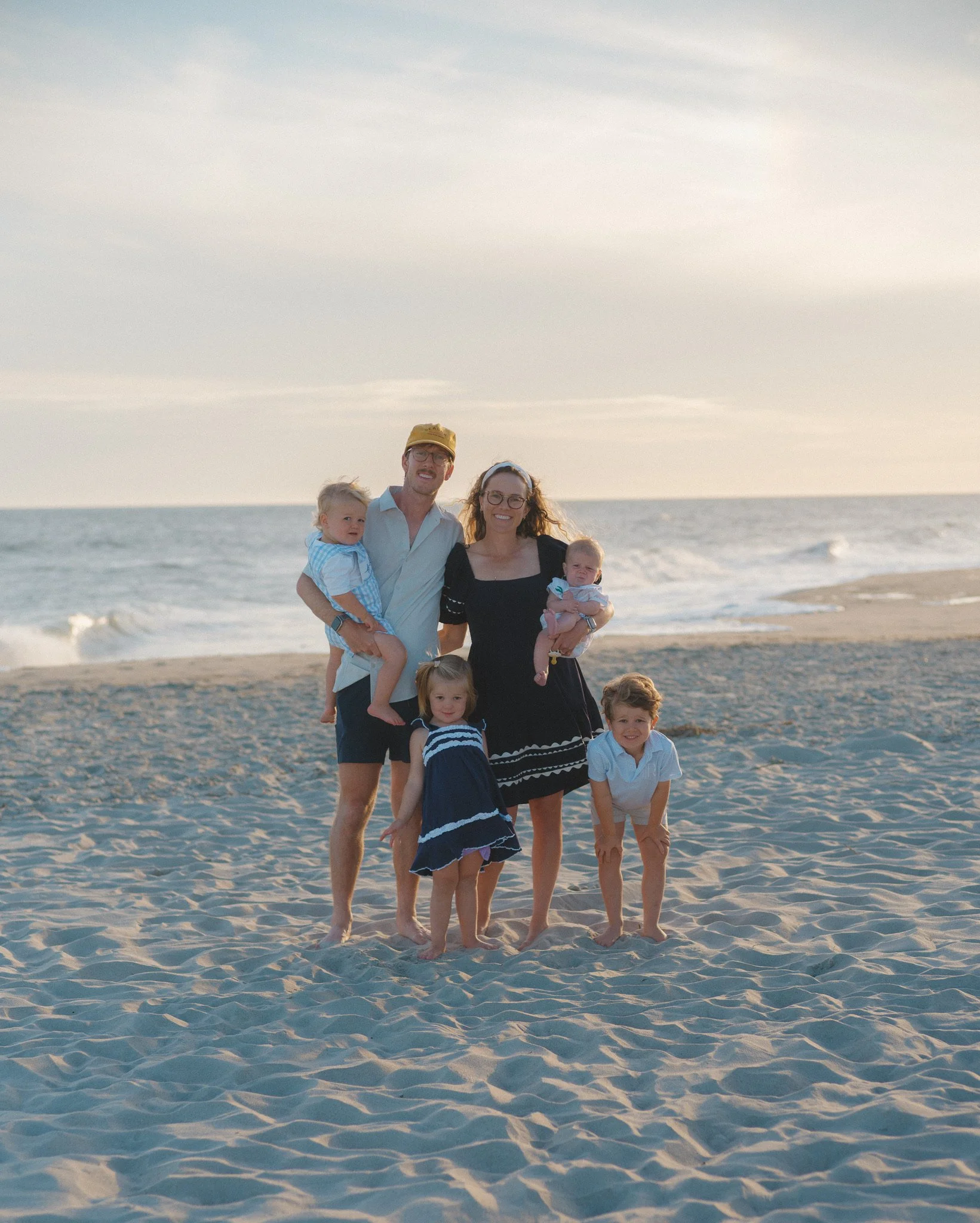 Family of six on the beach during sunset, with ocean waves in the background.
