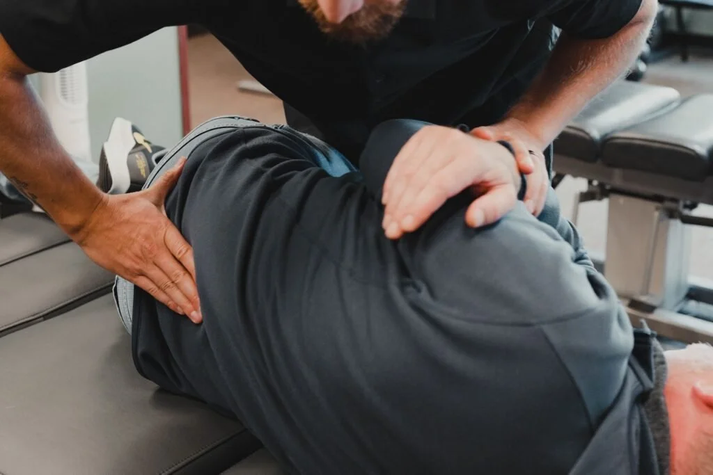 A person receiving chiropractic care, lying face down on a treatment table while a practitioner applies pressure to their lower back.