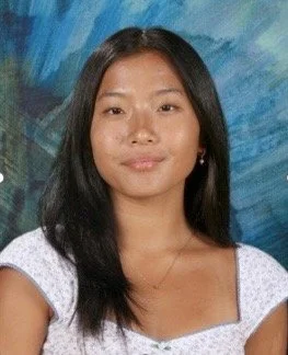 A woman with straight black hair wearing a white top, posing in front of a blue and green abstract background.