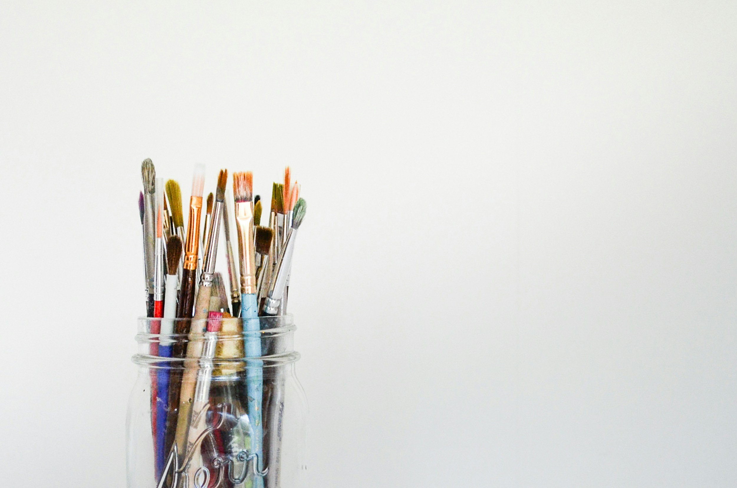 A glass jar filled with various paint brushes against a plain white background.