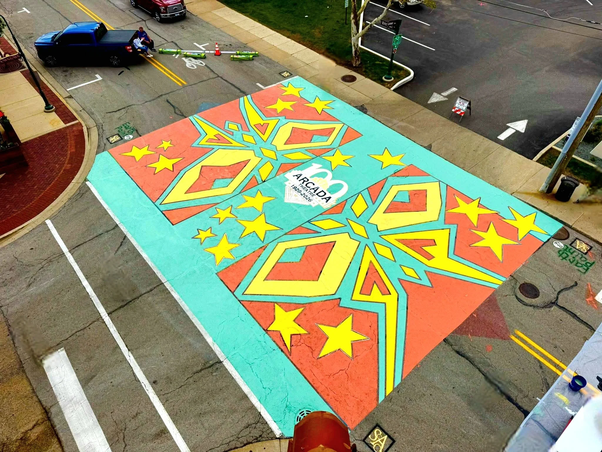A colorful mural painted on a sidewalk featuring a large star with smaller stars surrounding it and the text '150 Arcade Theatre 1926-2026.'