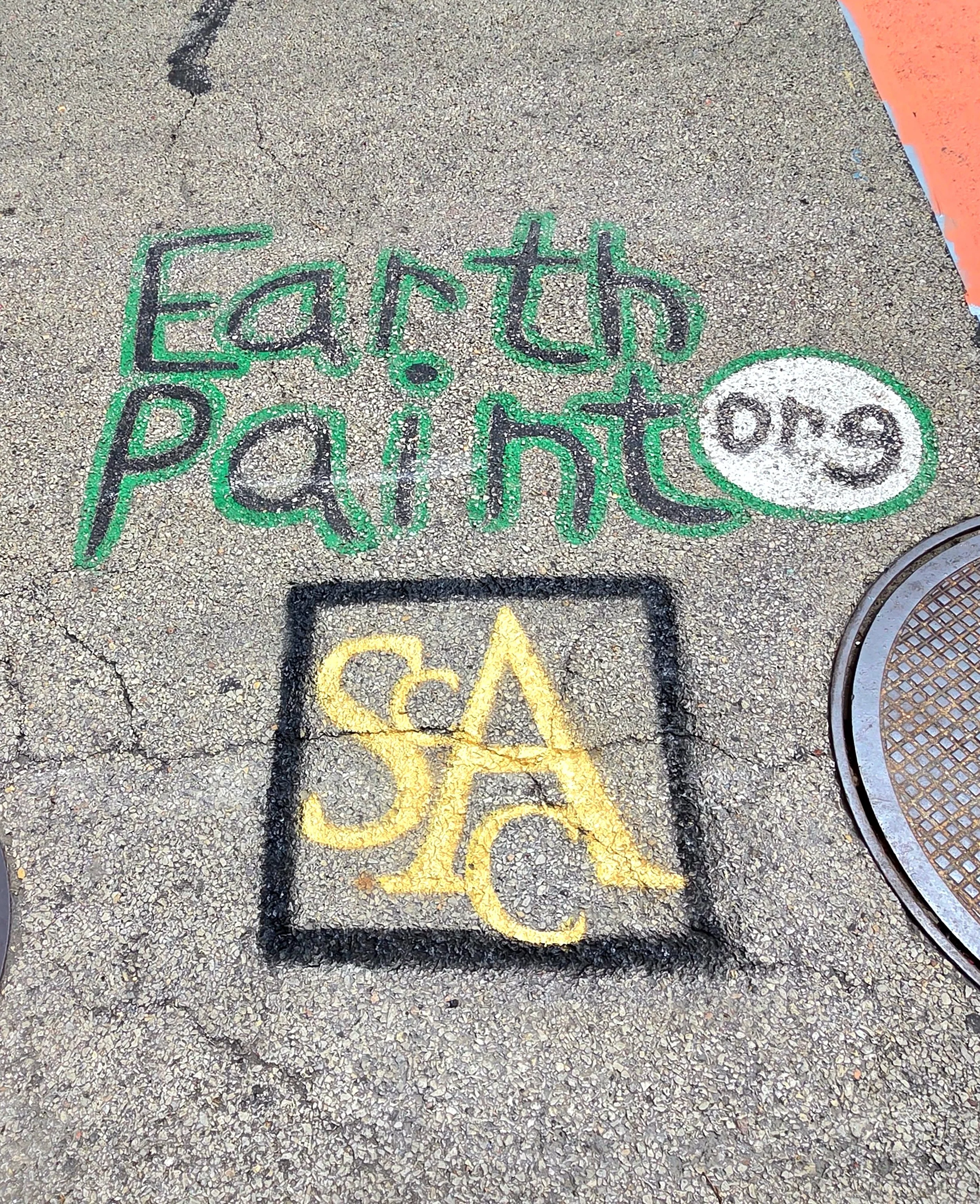 Colorful chalk writing on asphalt pavement. It says "Earth and Pet" with a smiley face in a speech bubble and the word "CA" in yellow.