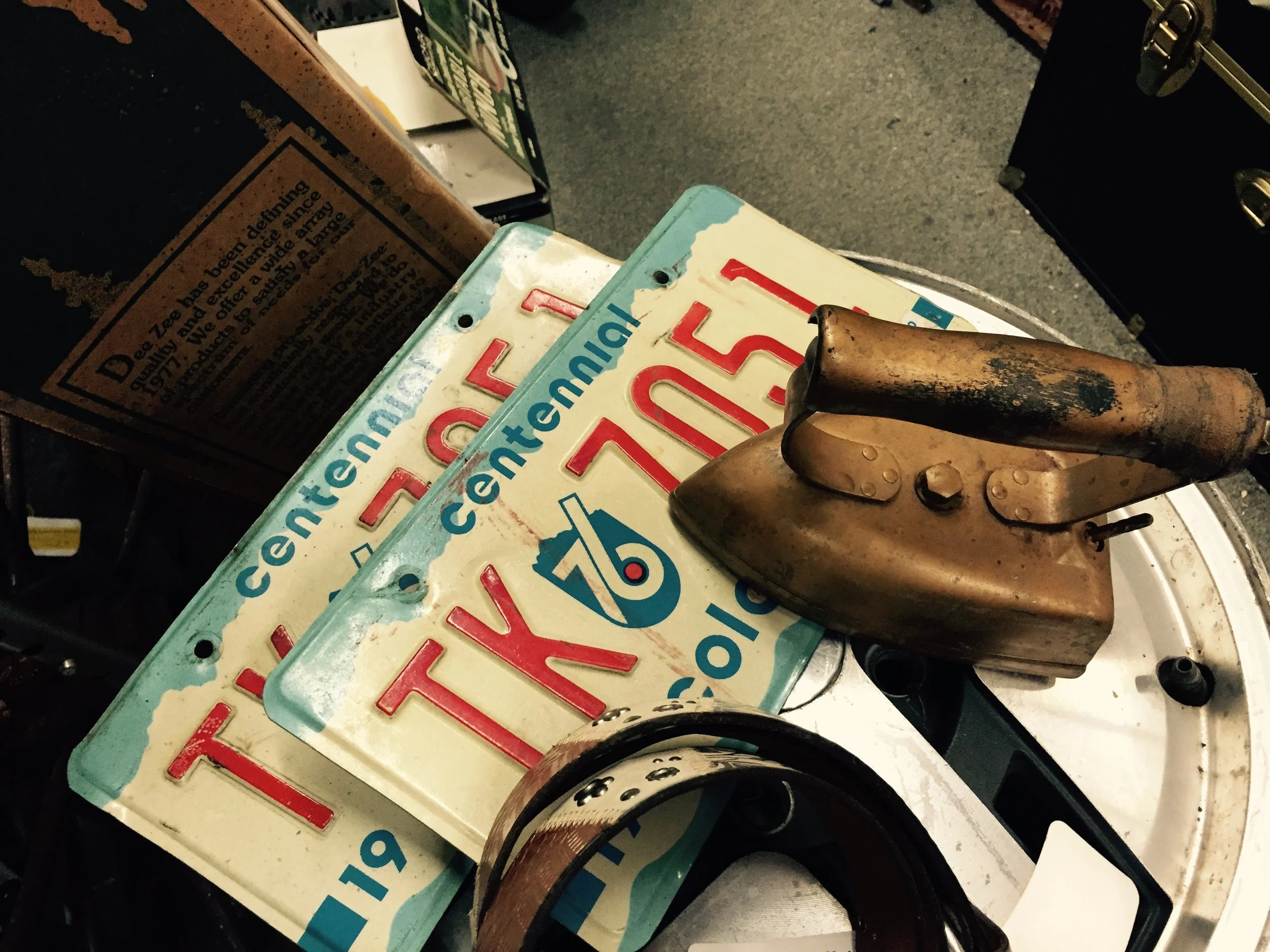 A rusty metal iron resting on top of two vintage Indiana license plates, near a cardboard box, on a table in a dimly lit room.