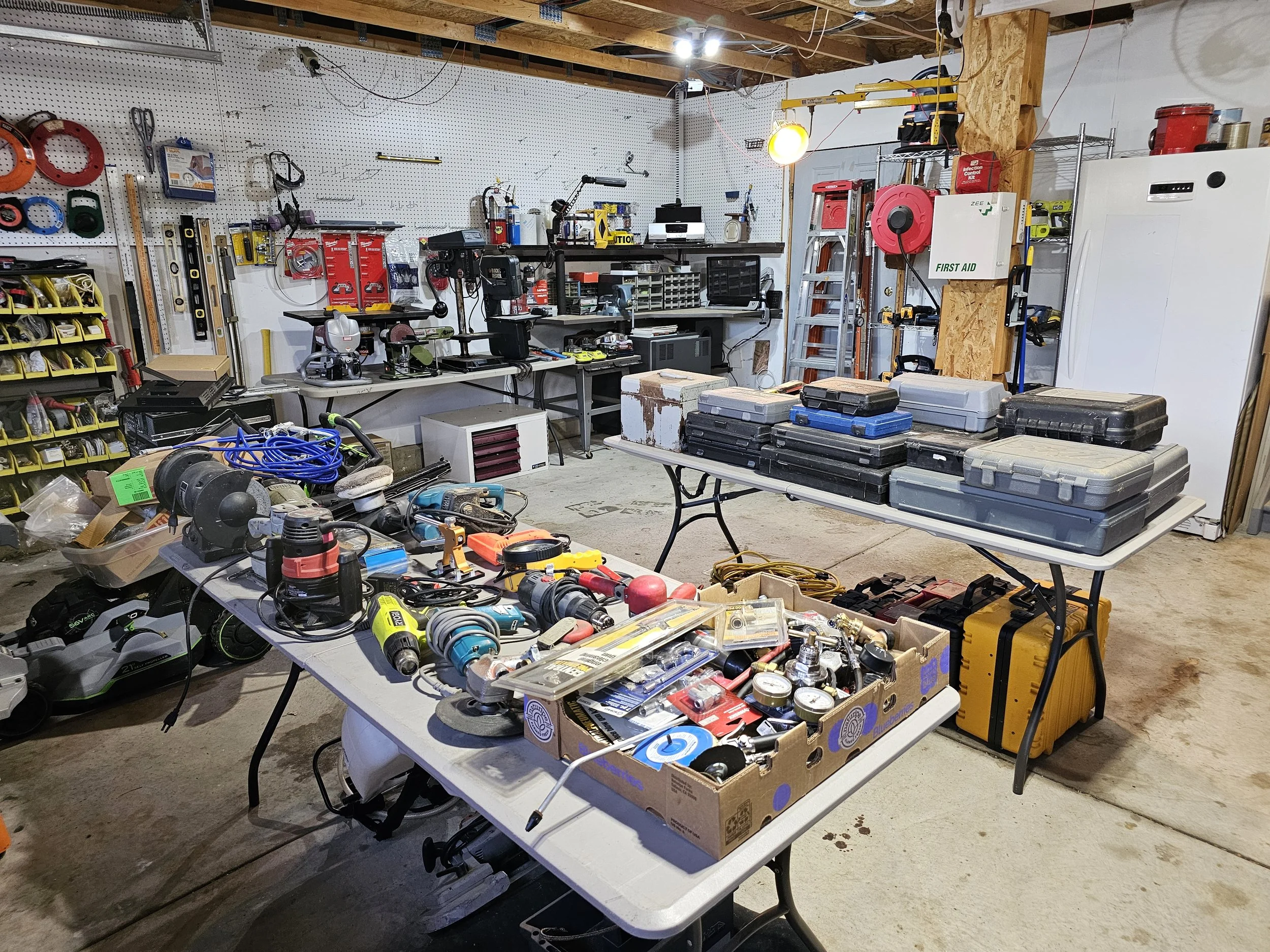 A well-organized workshop with tools, power equipment, and storage boxes on tables and shelves, featuring a pegboard with various hand tools and a wooden support beam.