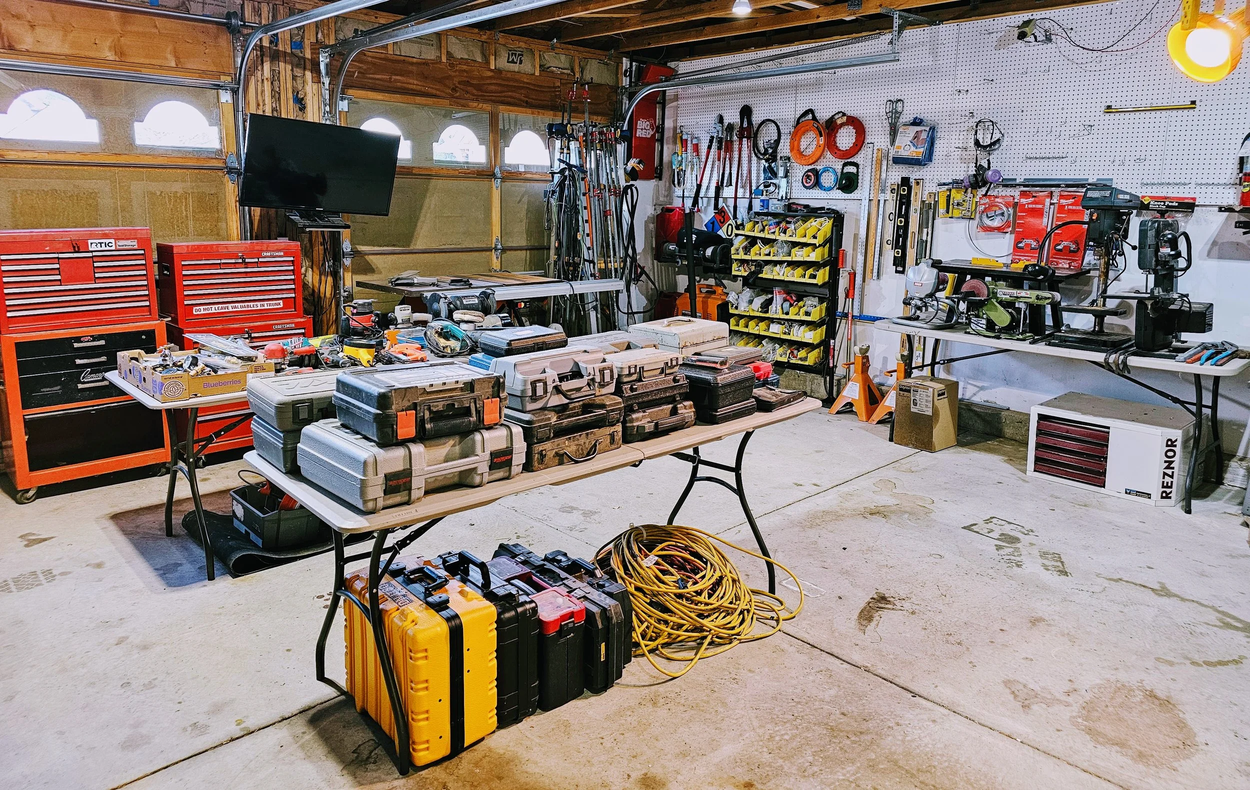 A well-organized garage workshop with red tool cabinets, portable tool cases on a table, and various power tools and equipment on shelves and workbenches.