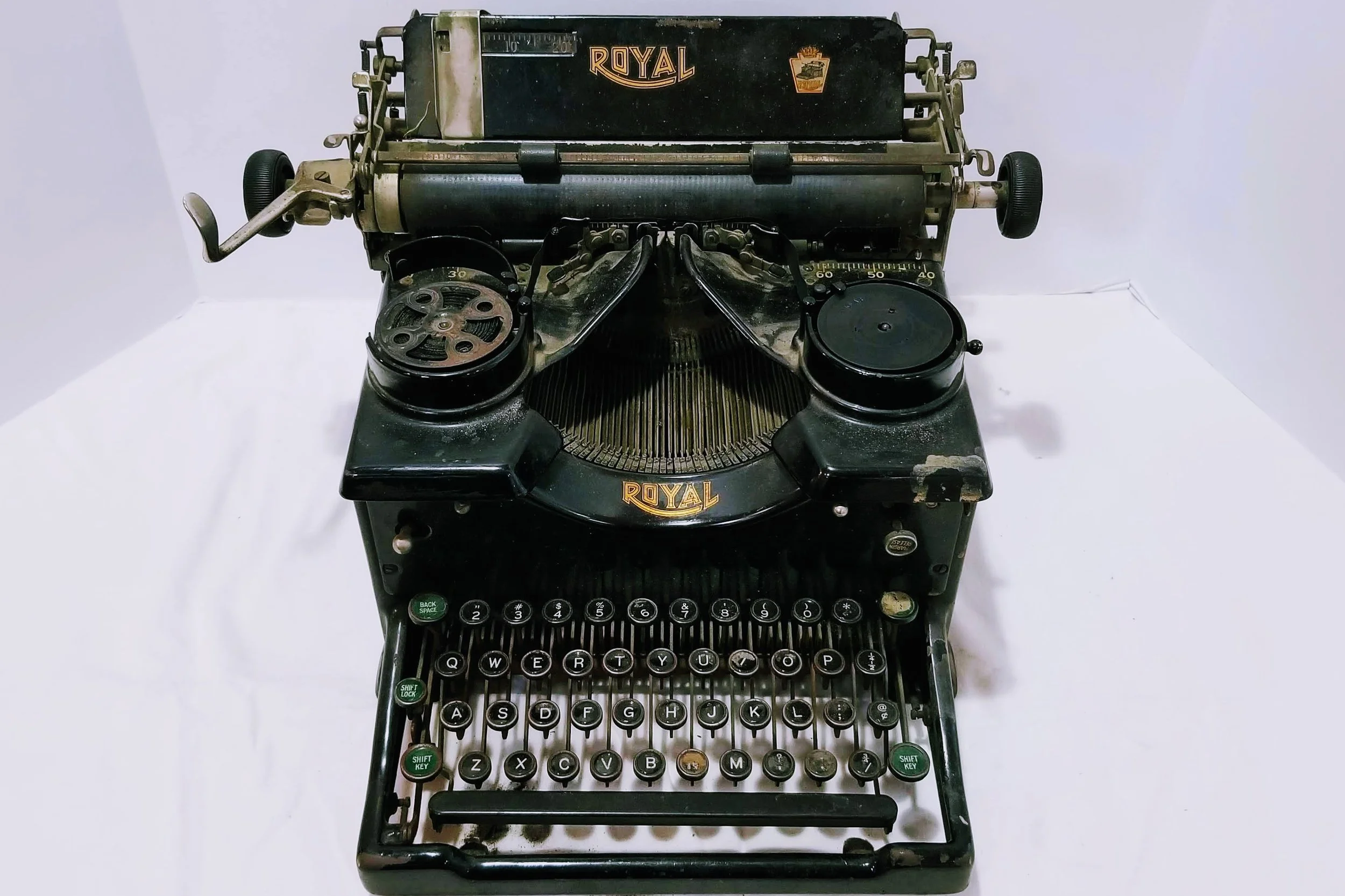 An antique black Royal typewriter with round keys, two large circular spools, and metal components, placed on a white surface against a plain background.
