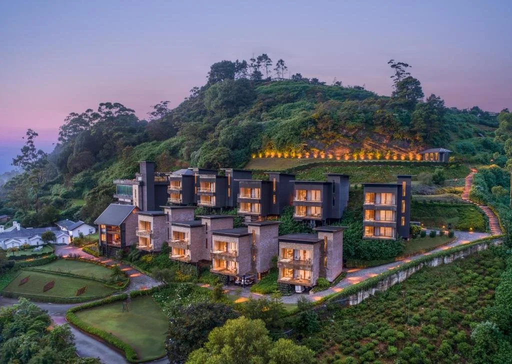 Luxury hillside resort with modern multi-story villas, lush greenery, garden pathways, and scenic mountain backdrop at dusk.