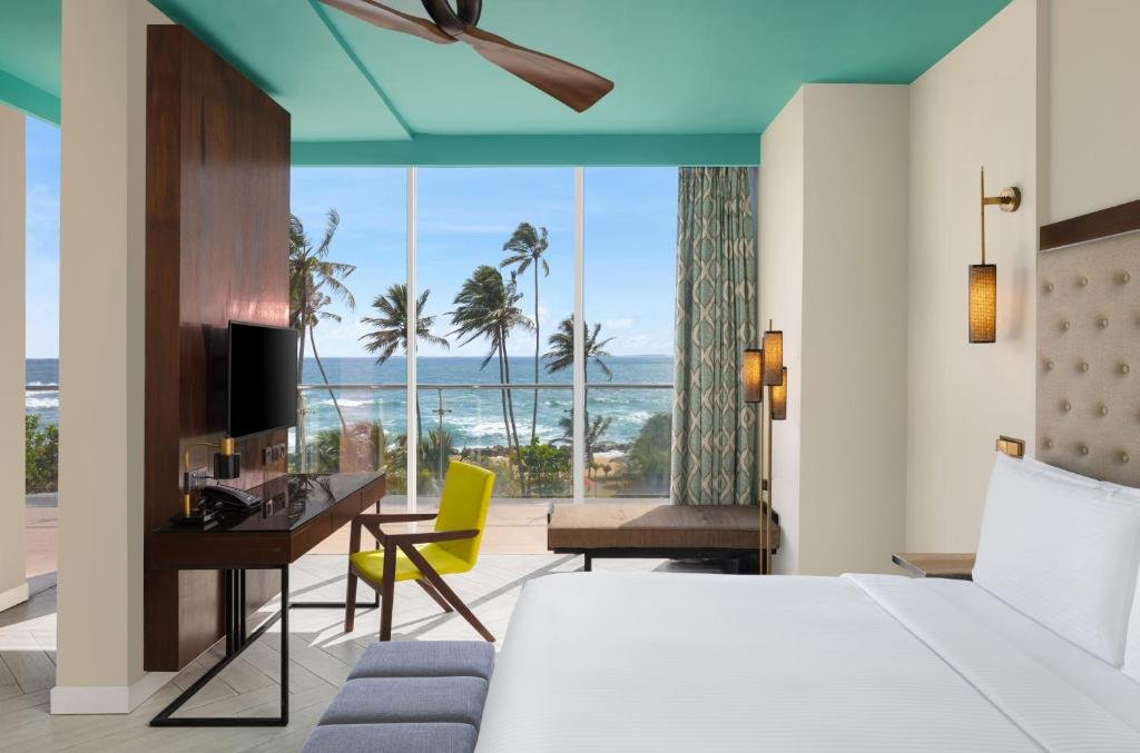 Hotel room with a view of the beach and palm trees outside the large glass window