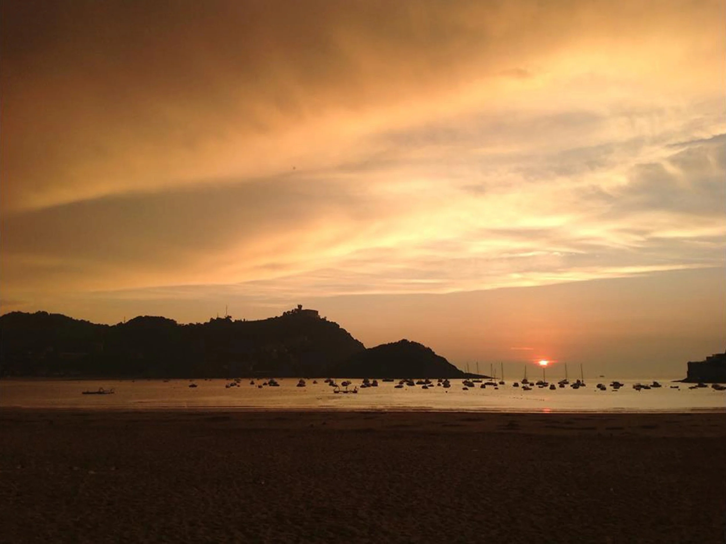 Sunset over a calm ocean with boats, a hilly coastline, and a colorful sky, in Sri Lanka