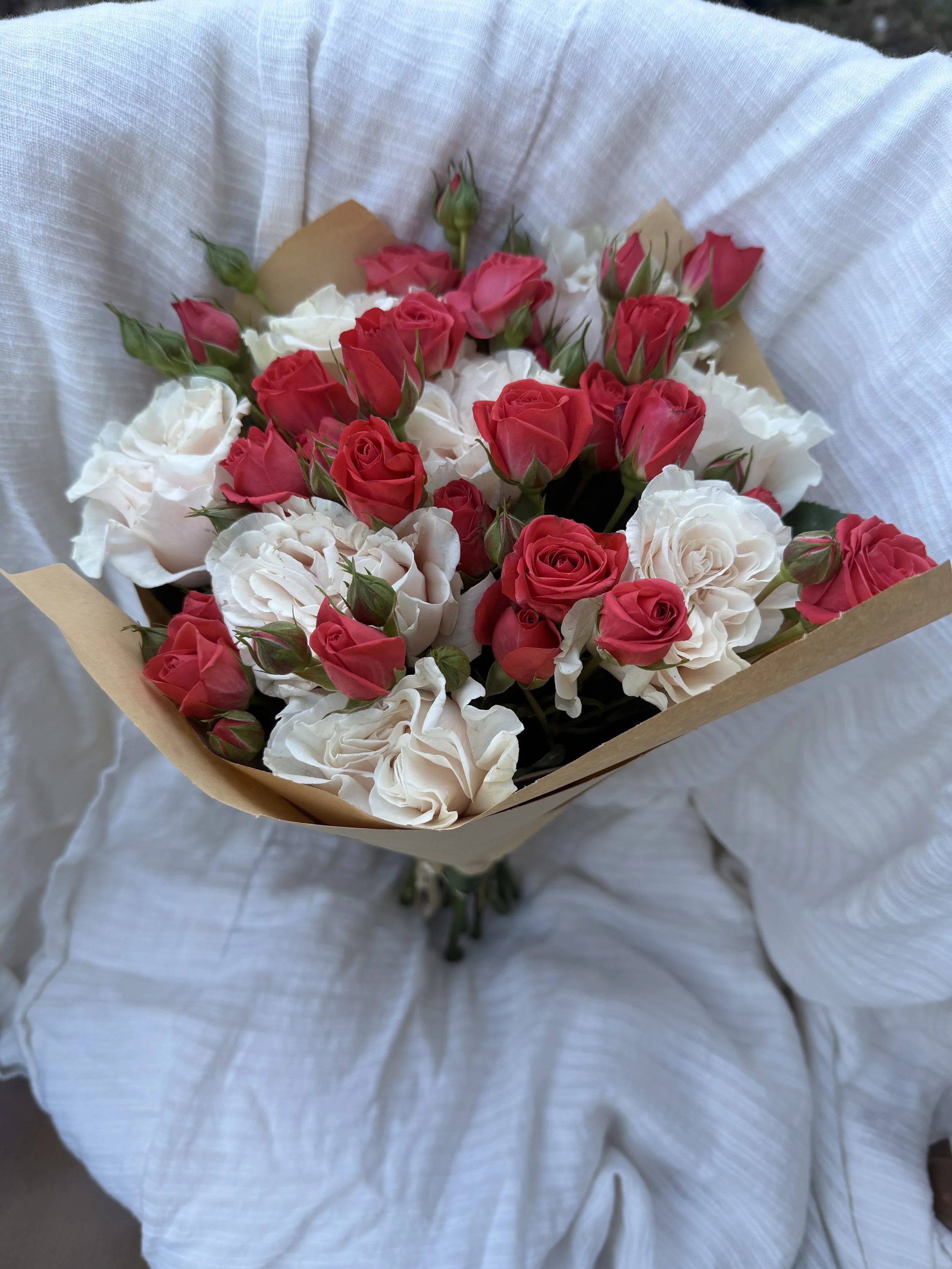 A bouquet of red and white roses being held by someone wearing a white textured dress or shirt.