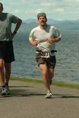 Male runner with bib number 2034 running along a lakeside walkway during daytime.