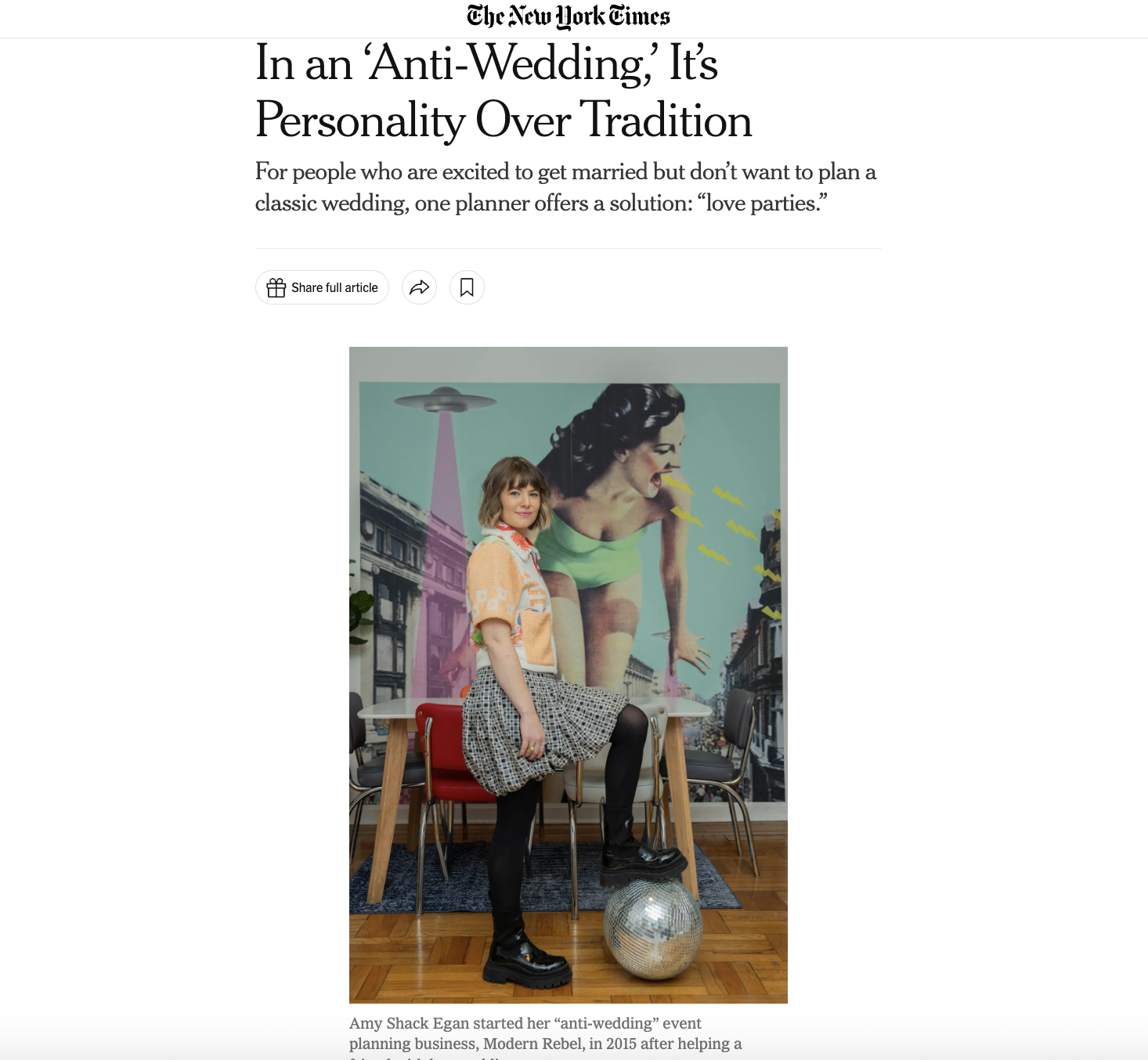 A woman with shoulder-length hair wearing a patterned skirt, black tights, black boots, and an orange patterned top standing inside a room. She is posing with her foot on a disco ball on the floor. Behind her is a mural of a woman with black hair in a green outfit, being lifted by a flying saucer above a city street scene.