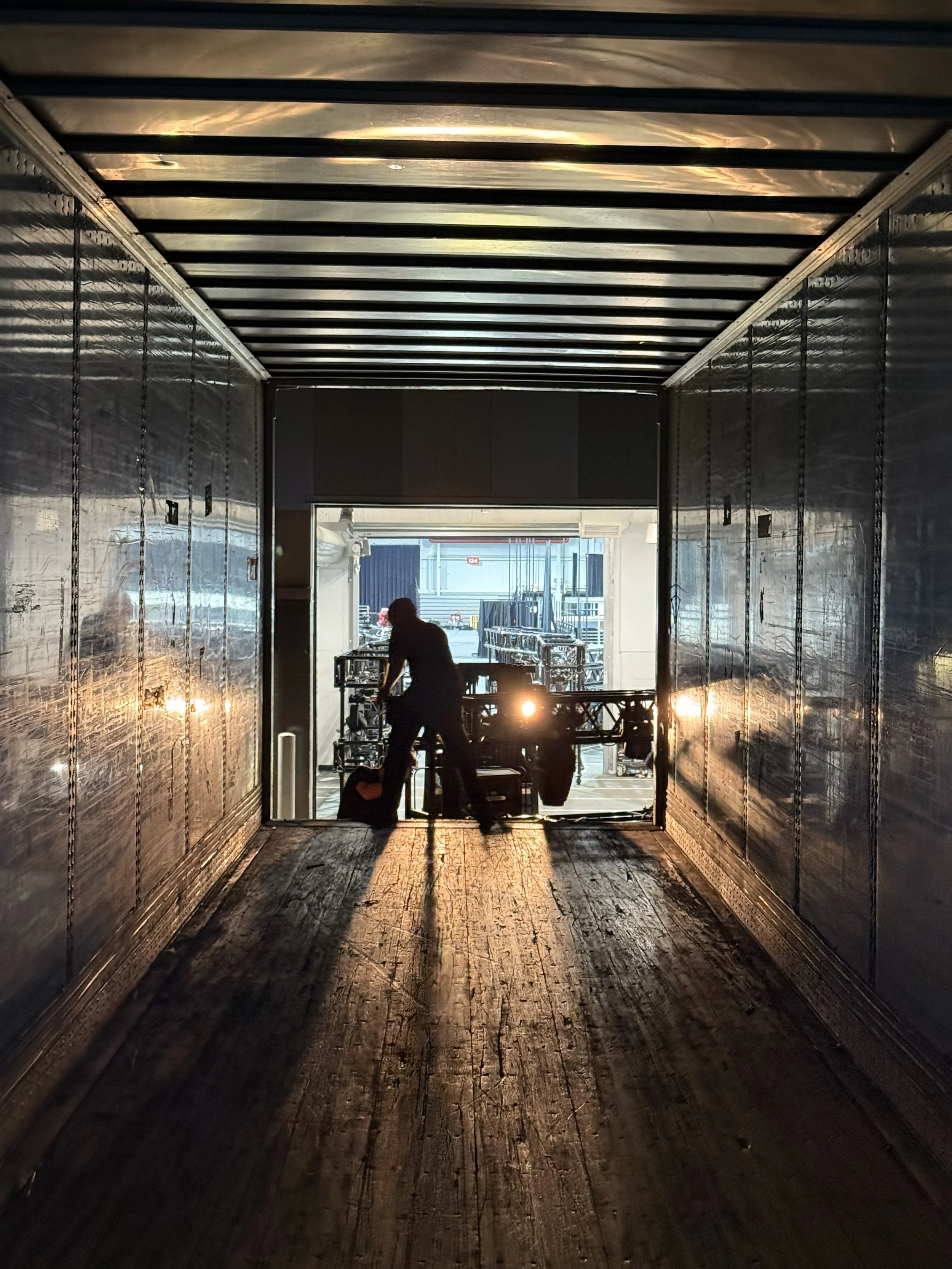 Silhouette of a person working on equipment in a loading dock with sunlight shining from an open background.