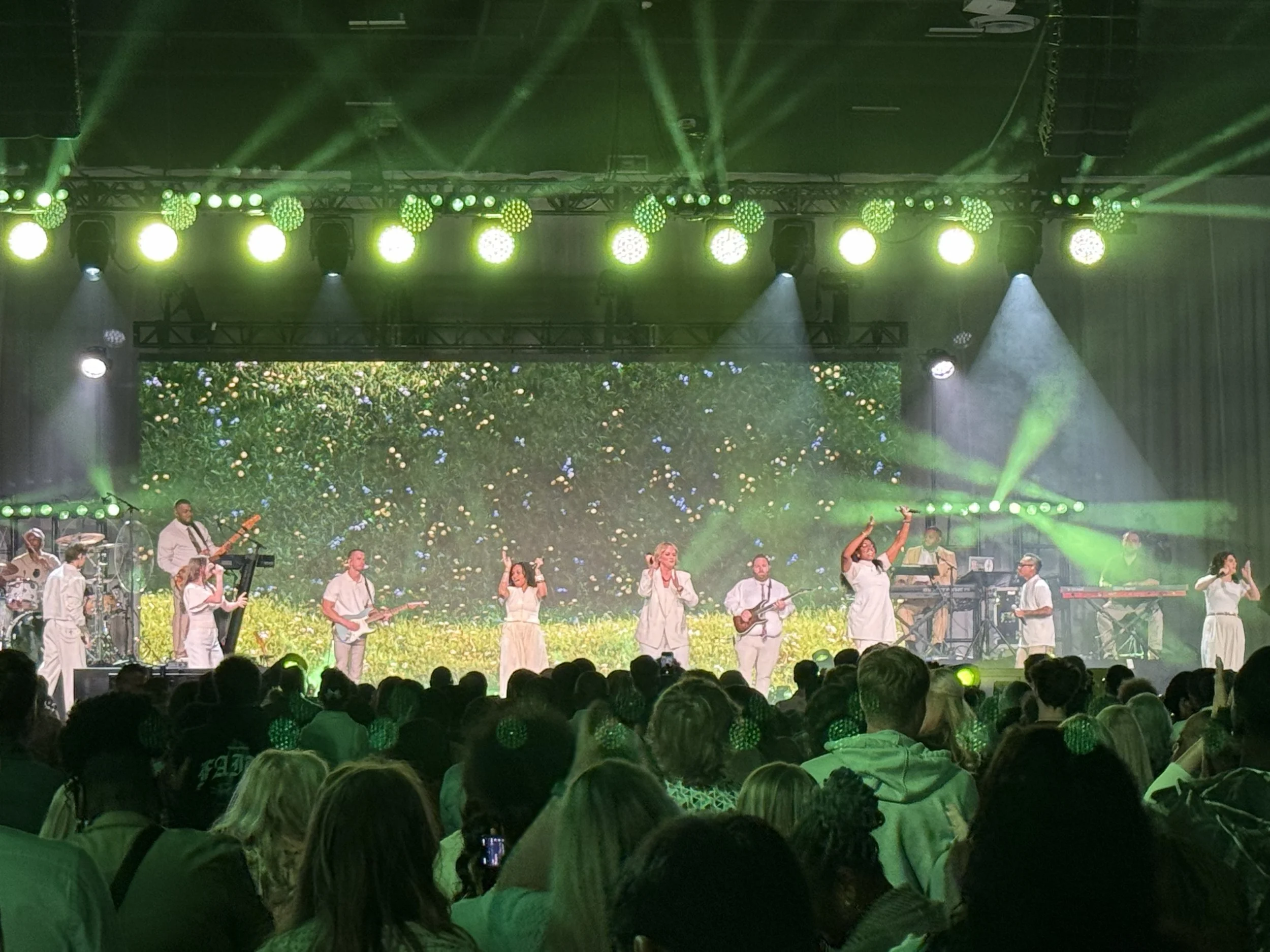 Group of musicians and performers in front of large scale led video wall and green lights.