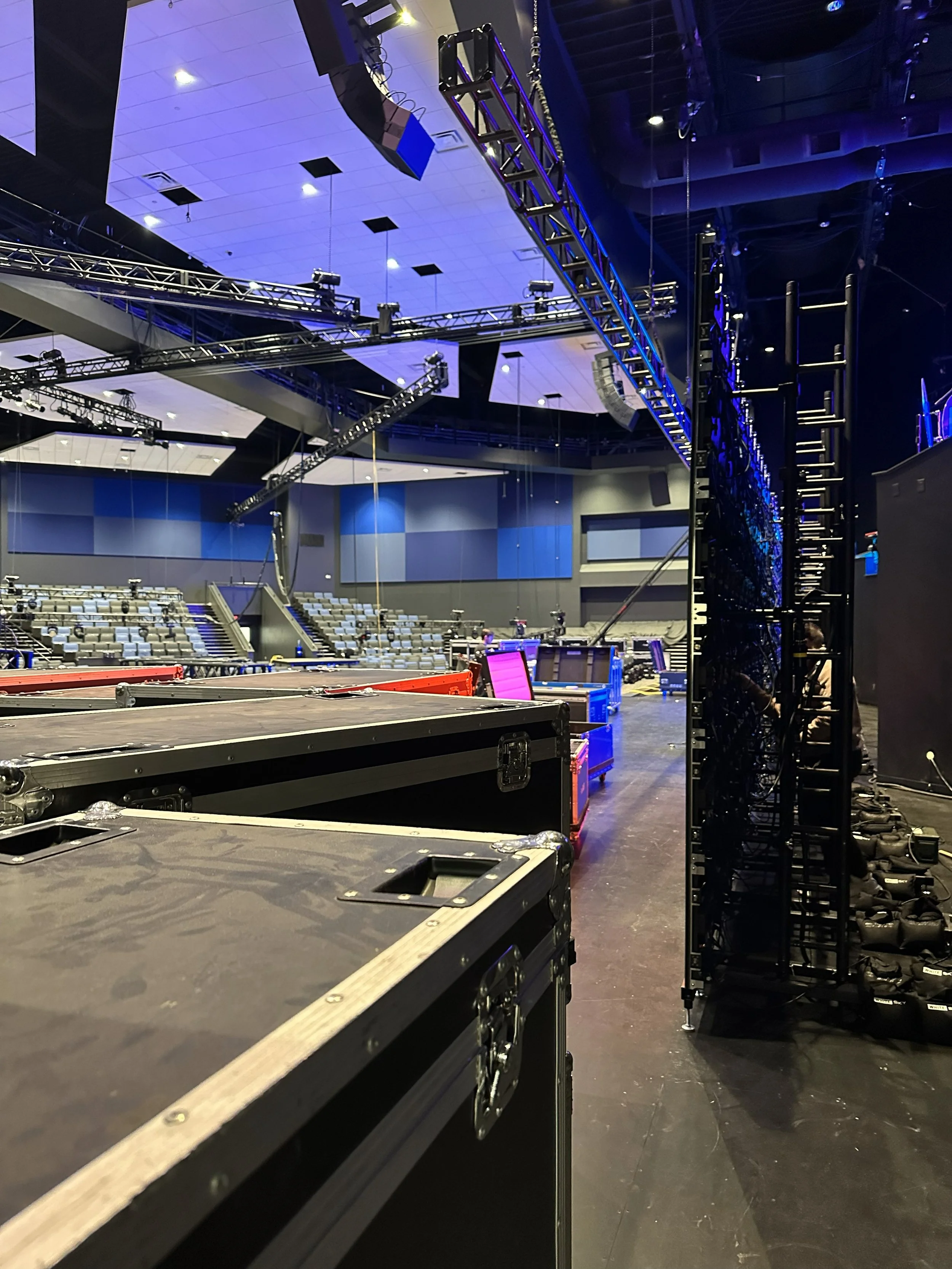 Interior of a large conference or concert hall with stage equipment, lighting rig, and empty seating area.