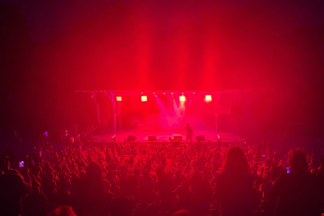 A rapper on stage at an outdoor concert performs under red stage lighting for a large audience.