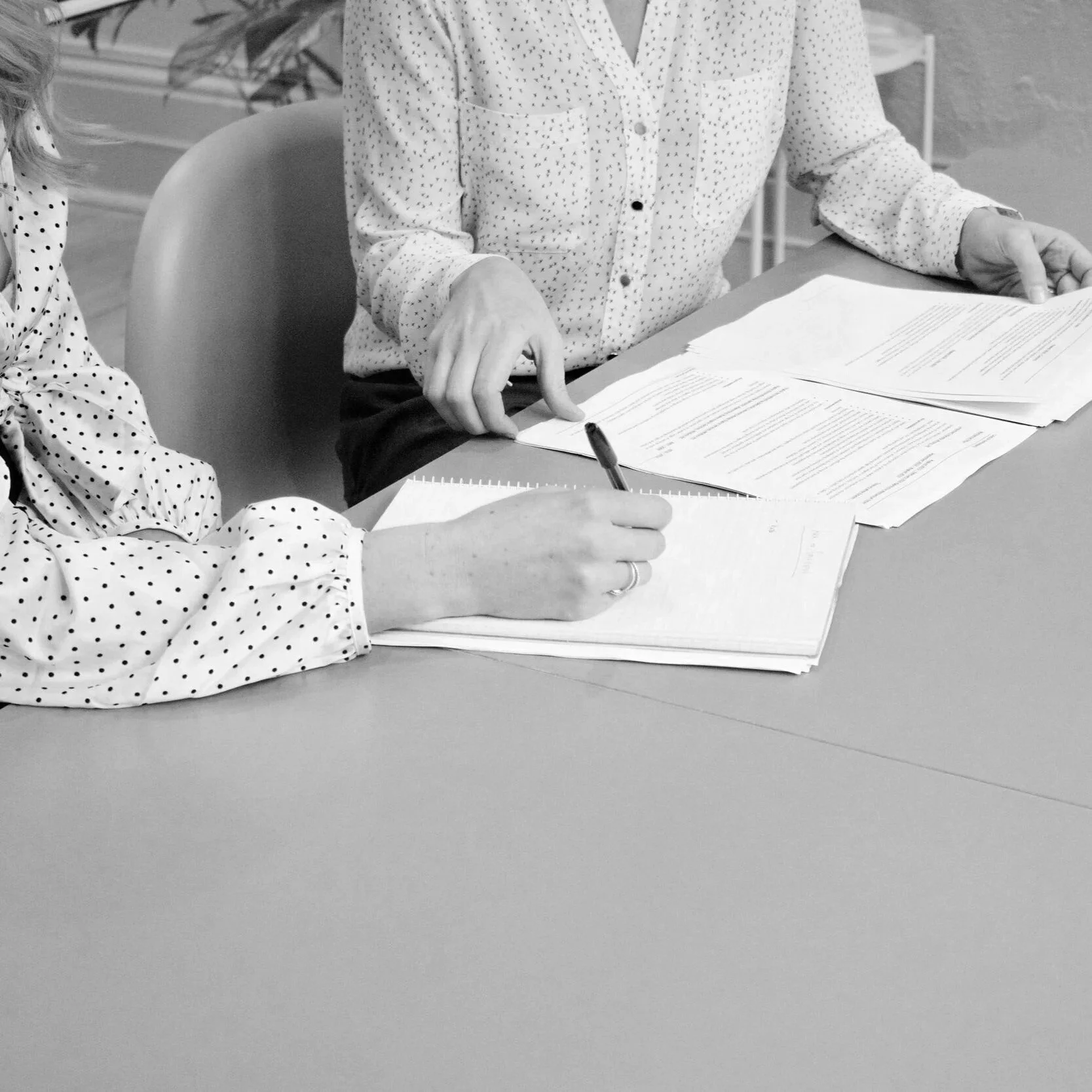 Two people sitting at a table reviewing and signing documents, with one person writing in a notepad.