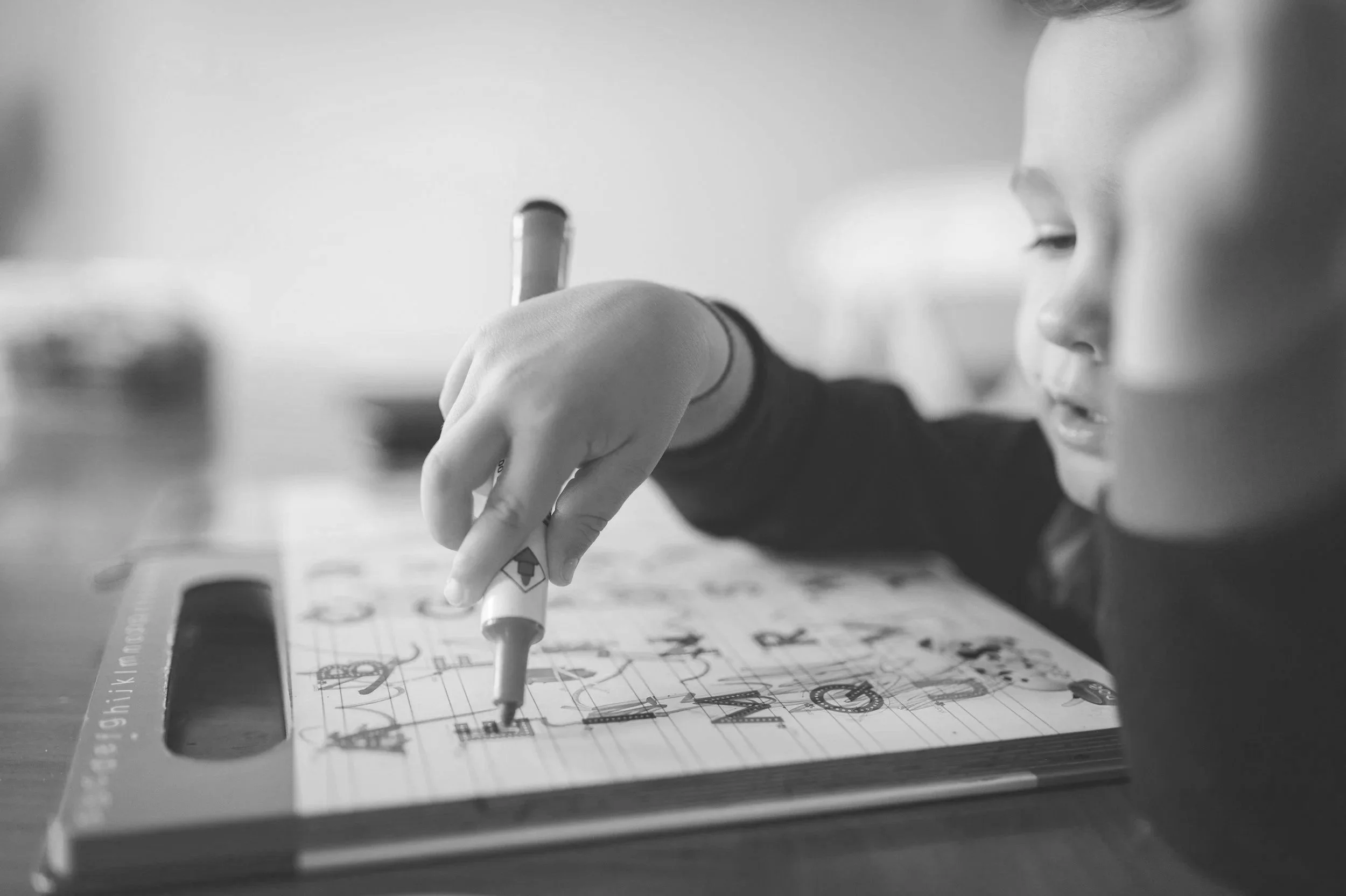 Child drawing or writing on a colorful educational worksheet with a marker, sitting at a desk.