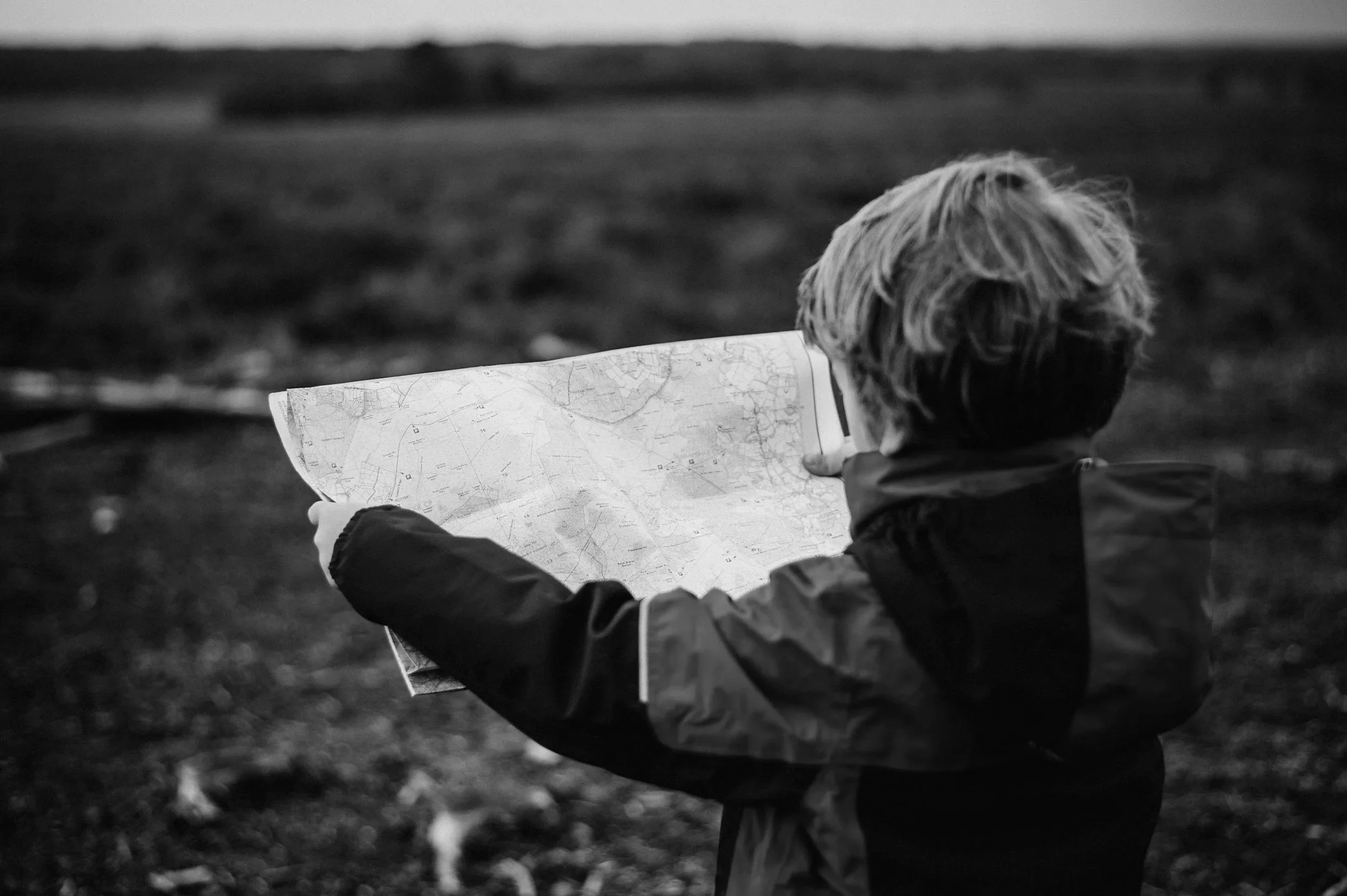 Child holding a map outdoors in a field with hills in the background, black and white photo.