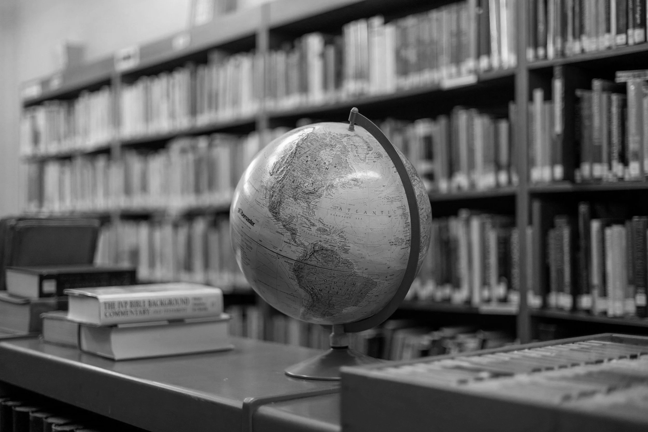 A globe on a table in a library with shelves of books in the background.