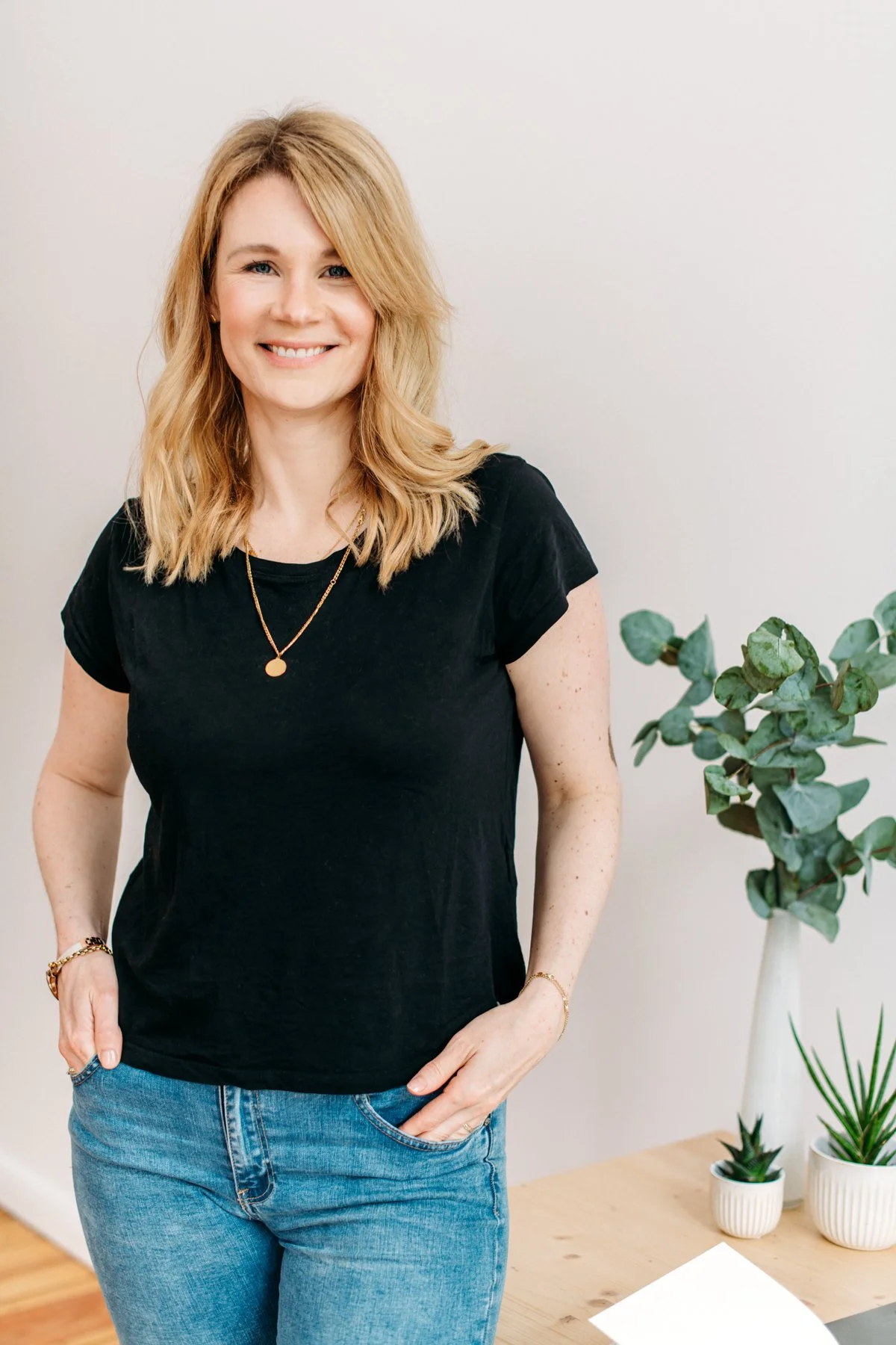 A woman with blonde hair and a black t-shirt standing next to a table with potted plants.