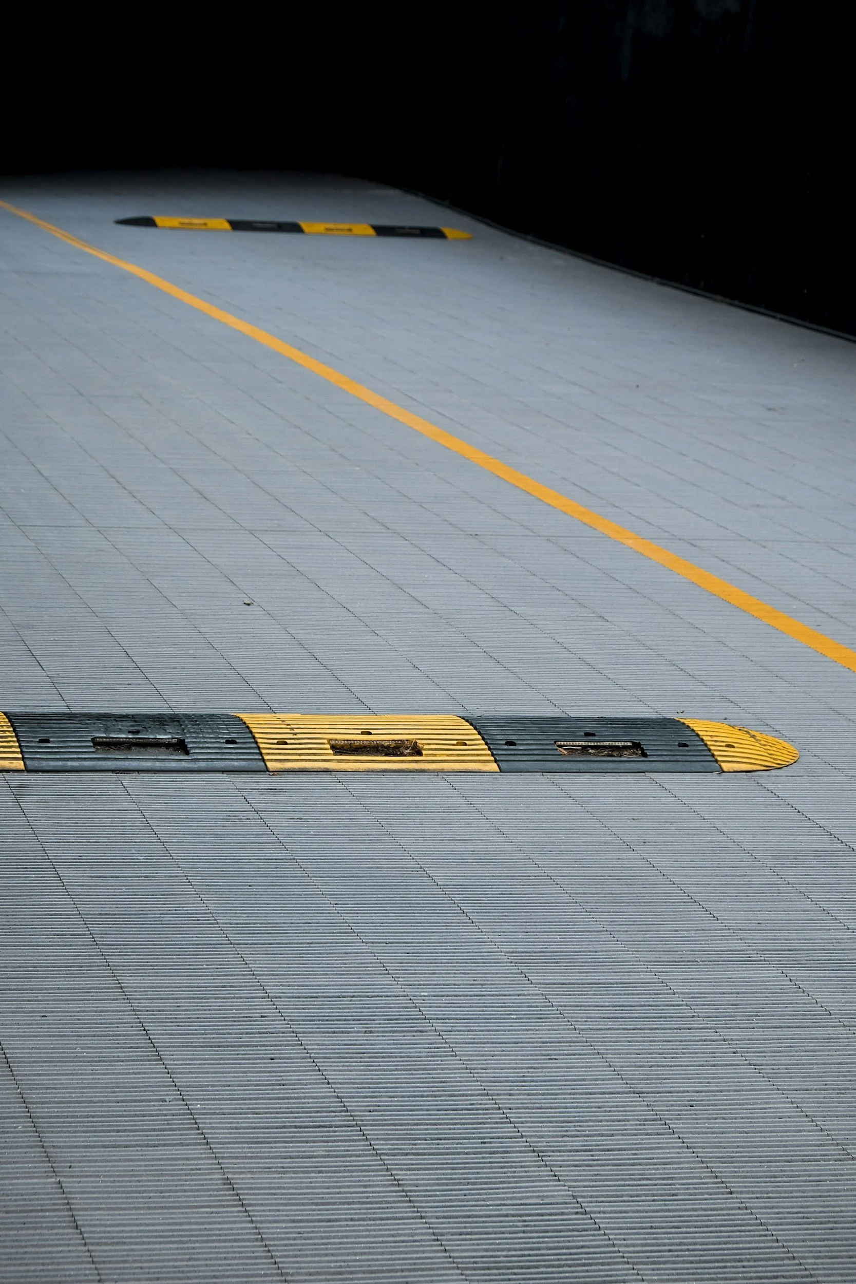 Empty parking garage ramp with yellow and black speed bumps and orange guiding lines