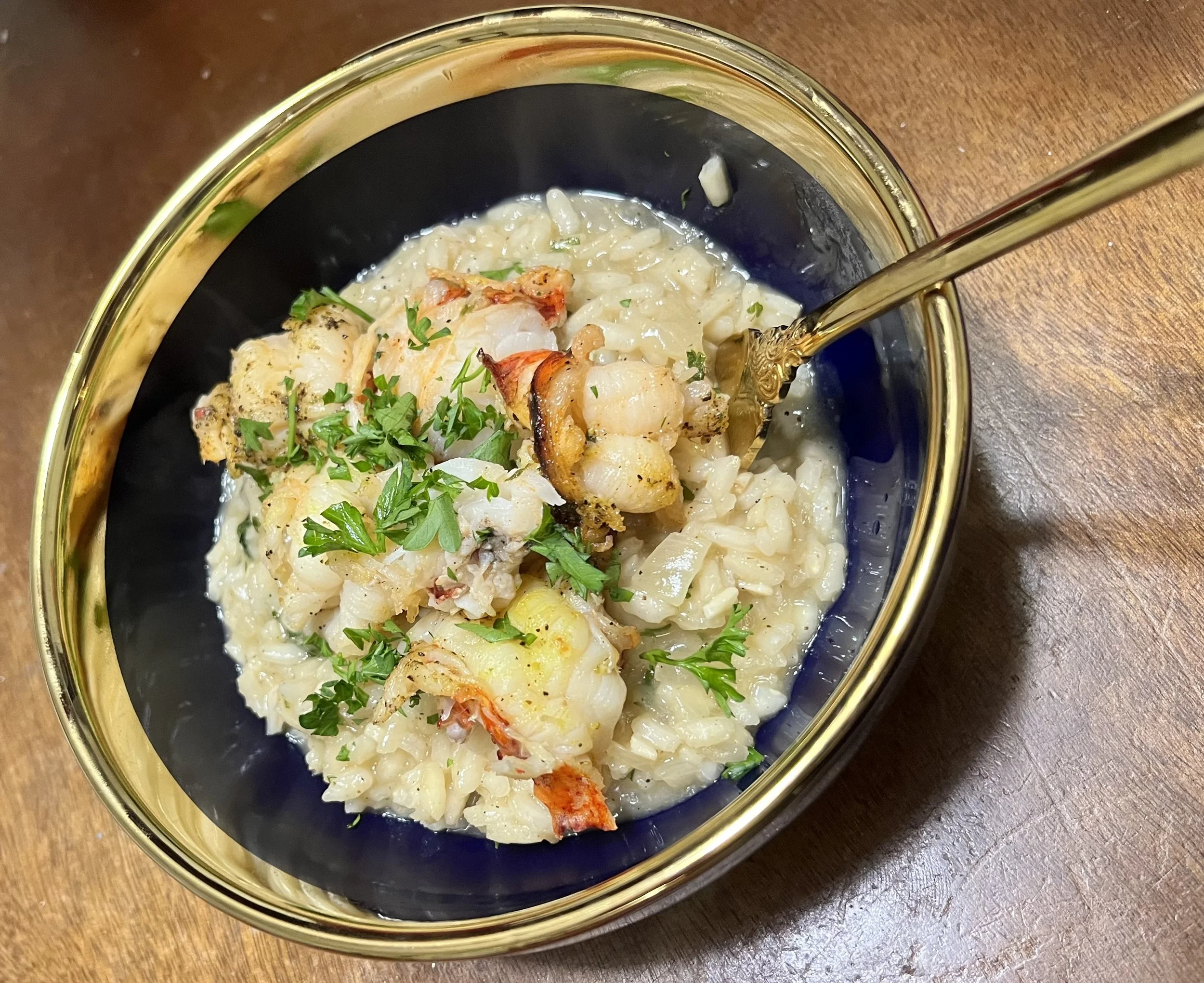 Lobster and shrimp risotto garnished with parsley in a black and gold bowl with a gold spoon