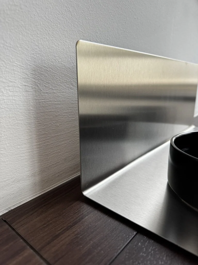 Nahaufnahme: DineShield Edelstahl-Napfunterlage in L-Form an der Wand – Spritzschutz für Wand und Boden