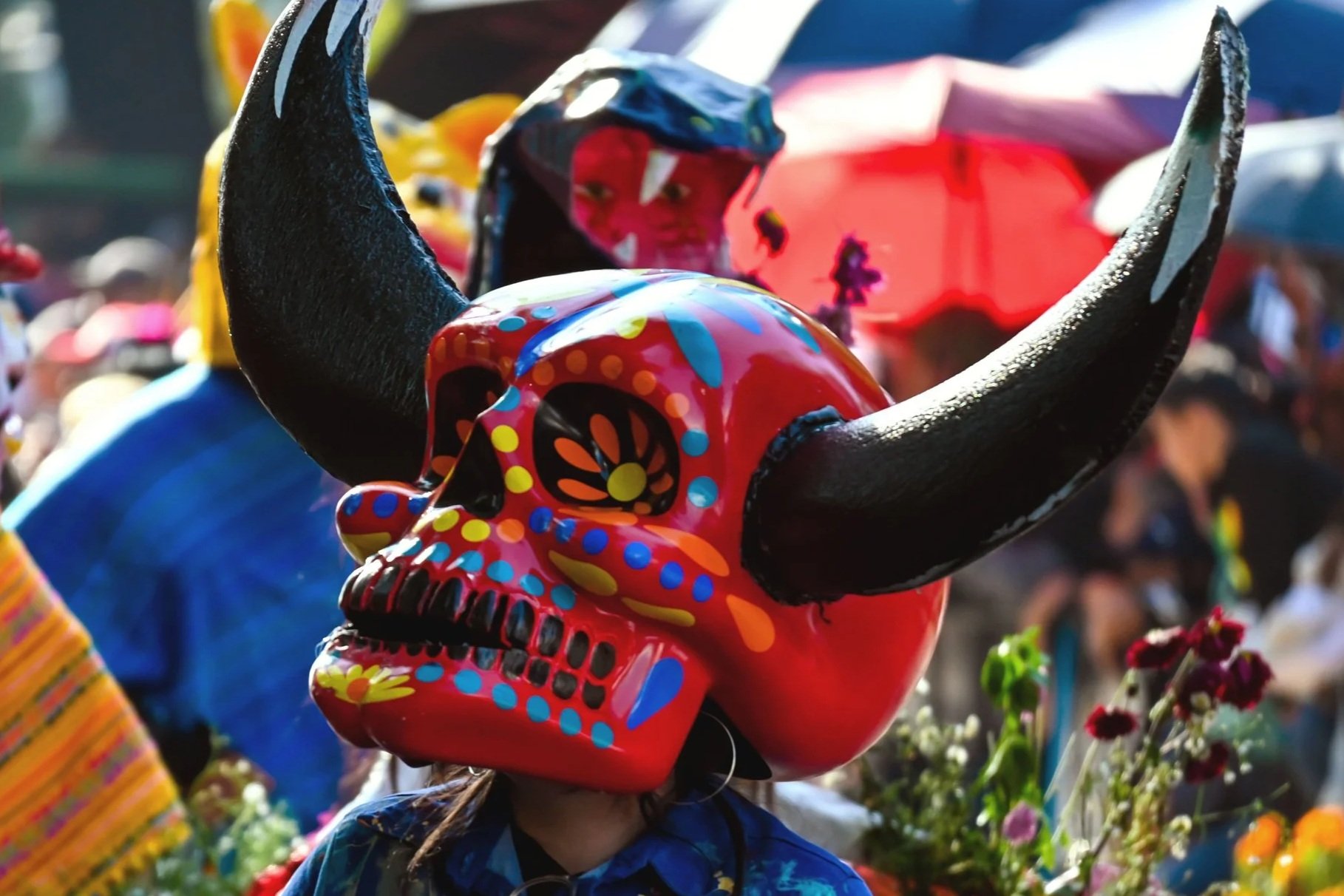 A person wearing a colorful skull mask with black horns during a celebration or festival.