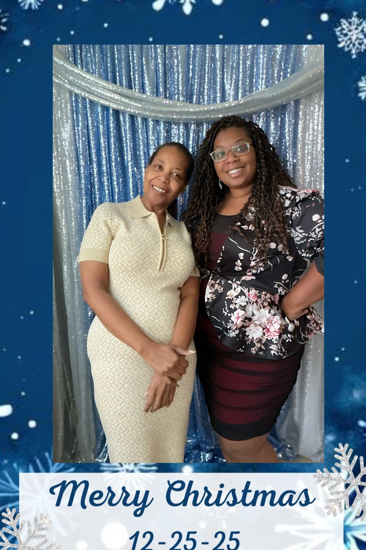 Two women standing together at Christmas celebration in front of a shiny blue and silver backdrop, smiling at the camera. The photo is framed with a holiday-themed border that says 'Merry Christmas 12-25-25' with snowflakes.