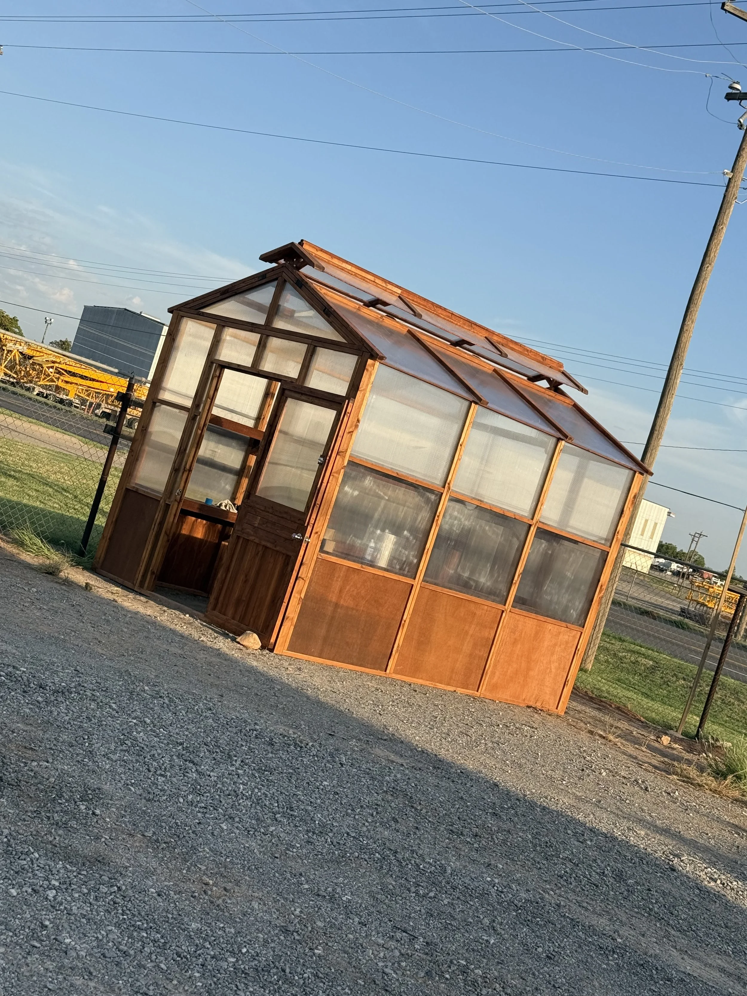 Stained cedar greenhouse on gravel with person at the door