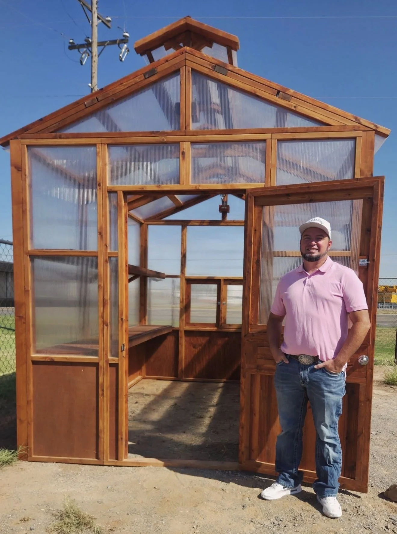 Man in pink shirt standing in the doorway of a cedar greenhouse