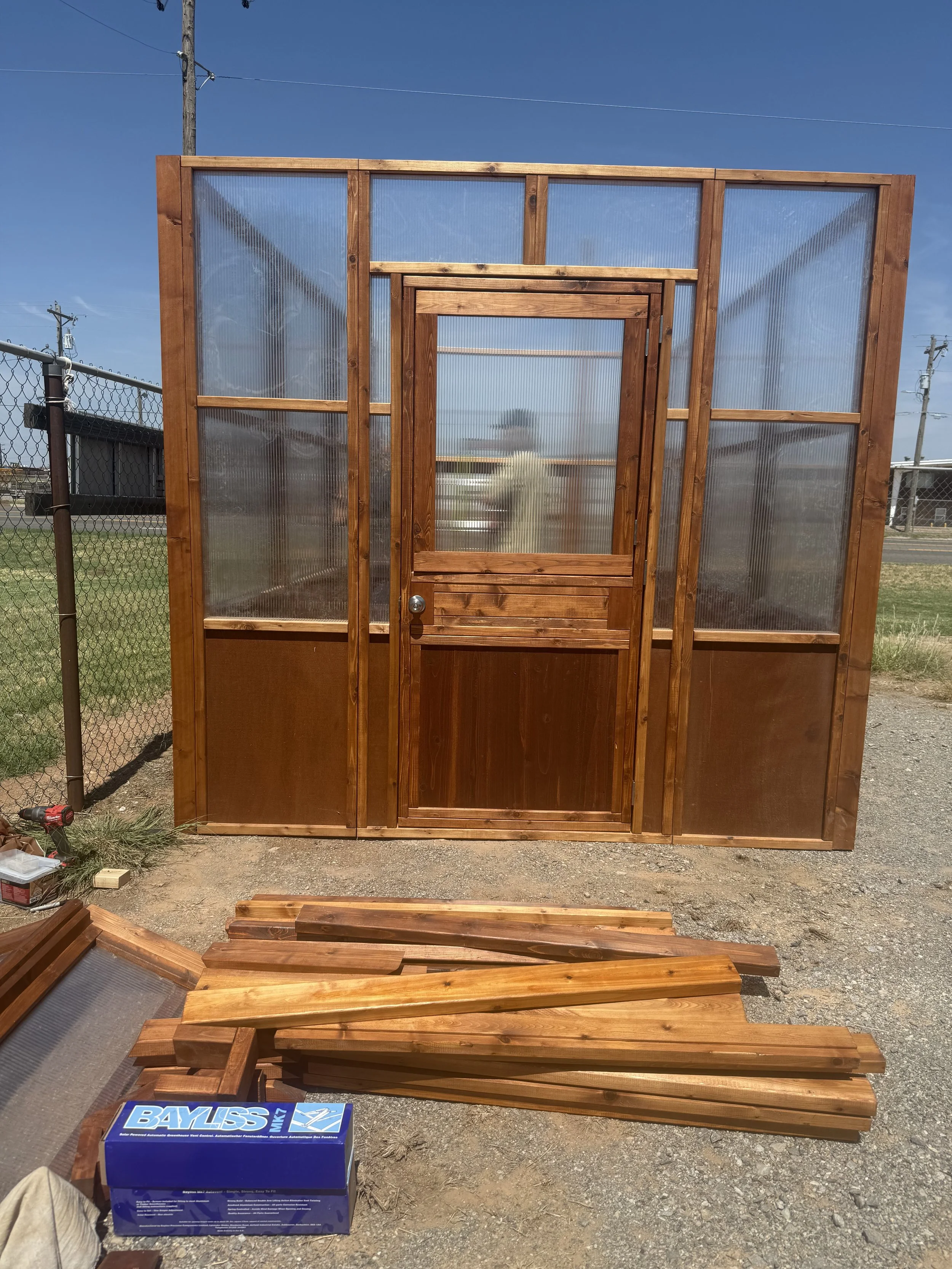 Cedar greenhouse with open door and stacked lumber in front