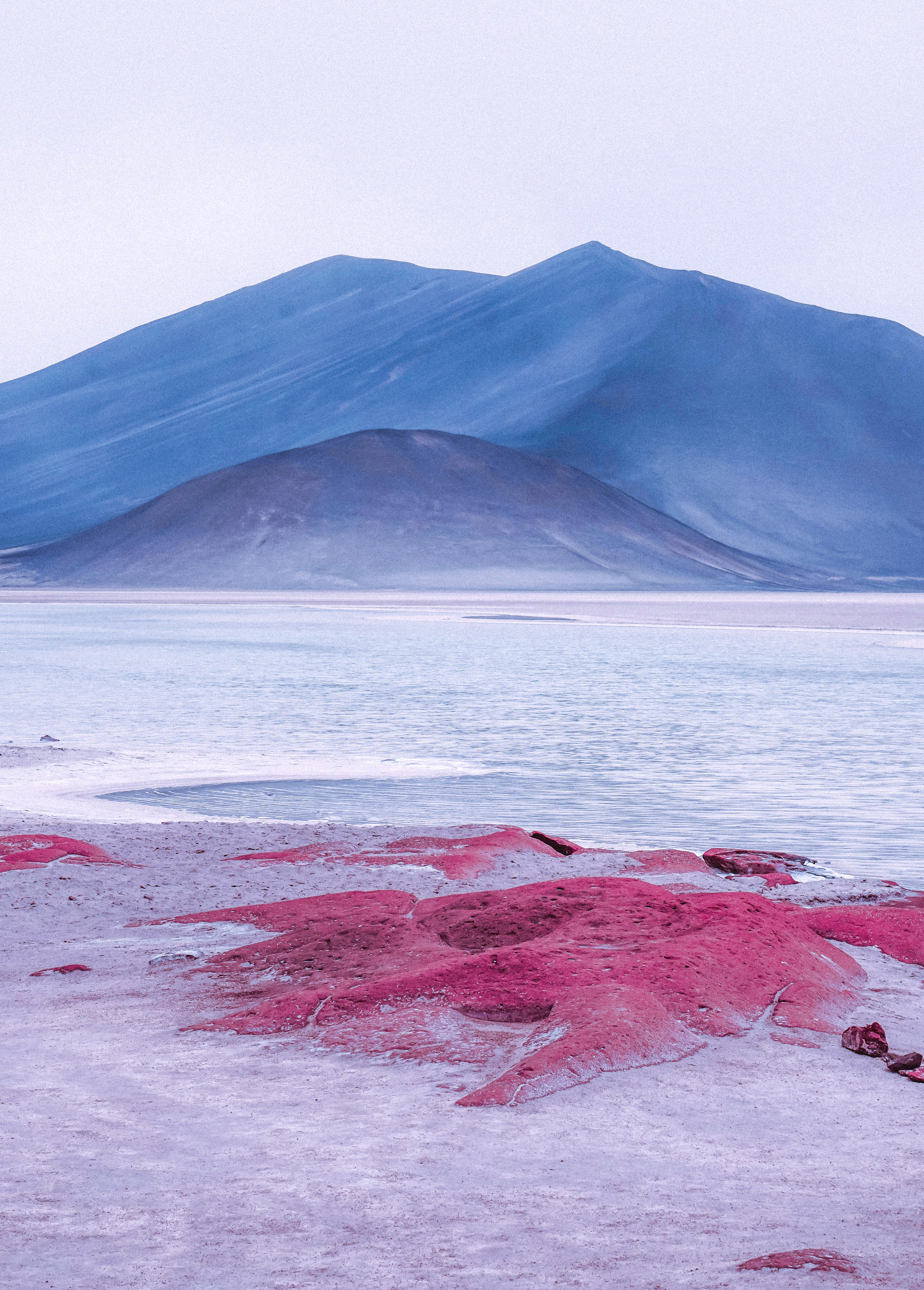 Photo of a salt flat with large red rocks in the foreground and blue mountains in the background