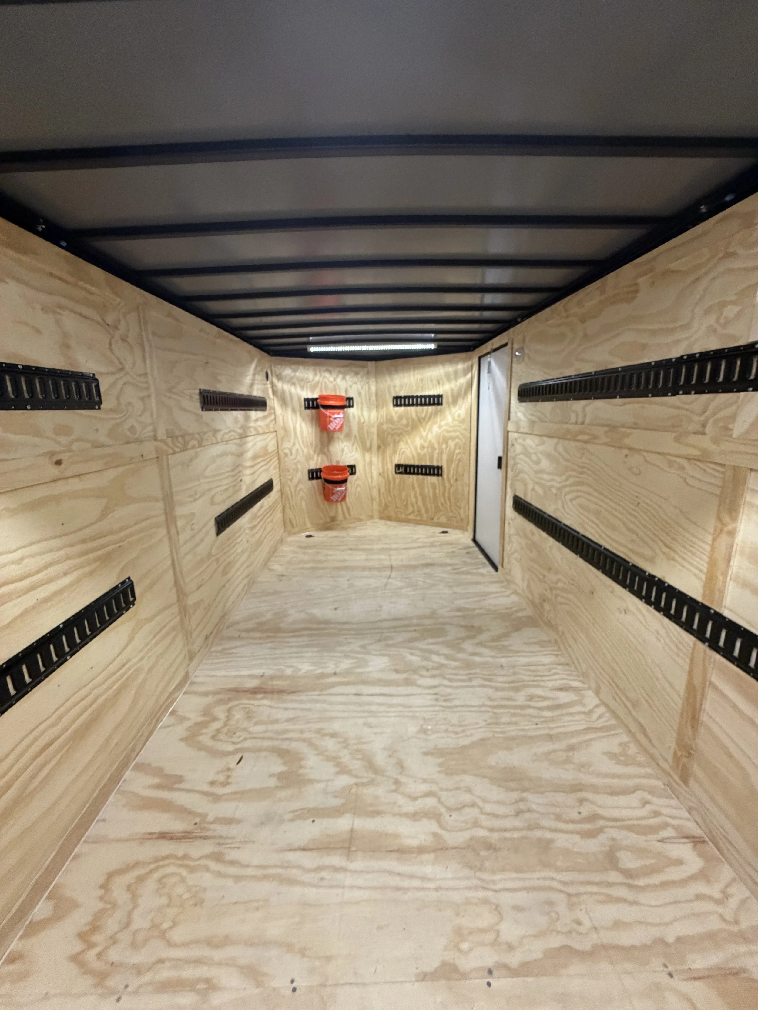 Empty trailer with wooden interior, black side rails, a door at the back, and two red buckets on the wall.