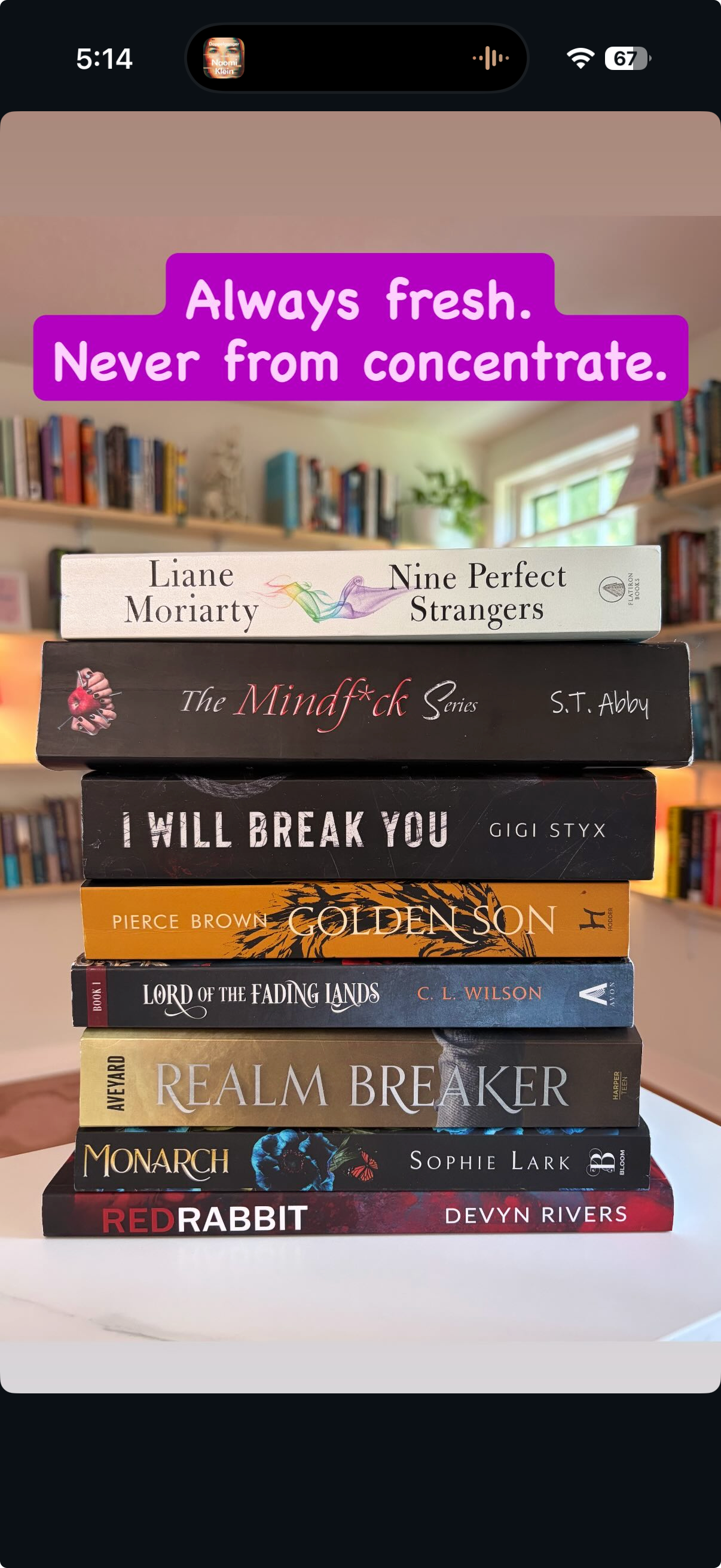 Stack of ten books on a white table in a room with bookshelves and window in the background. The books include 'Nine Perfect Strangers' by Liane Moriarty, 'The Mindf*ck Series' by S.T. Abby, 'I Will Break You' by Gigi STYX, 'Golden Son' by Pierce Brown, 'Lord of the Fading Lands' by C.L. Wilson, 'Realm Breaker' by Aya, 'Monarch' by Sophie Lark, and 'Red Rabbit' by Devyn Rivers. A purple text overlay reads: 'Always fresh. Never from concentrate.'